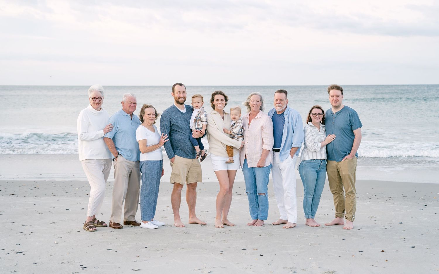 Multi-generational family portrait on beach in coordinating blue and white outfits.