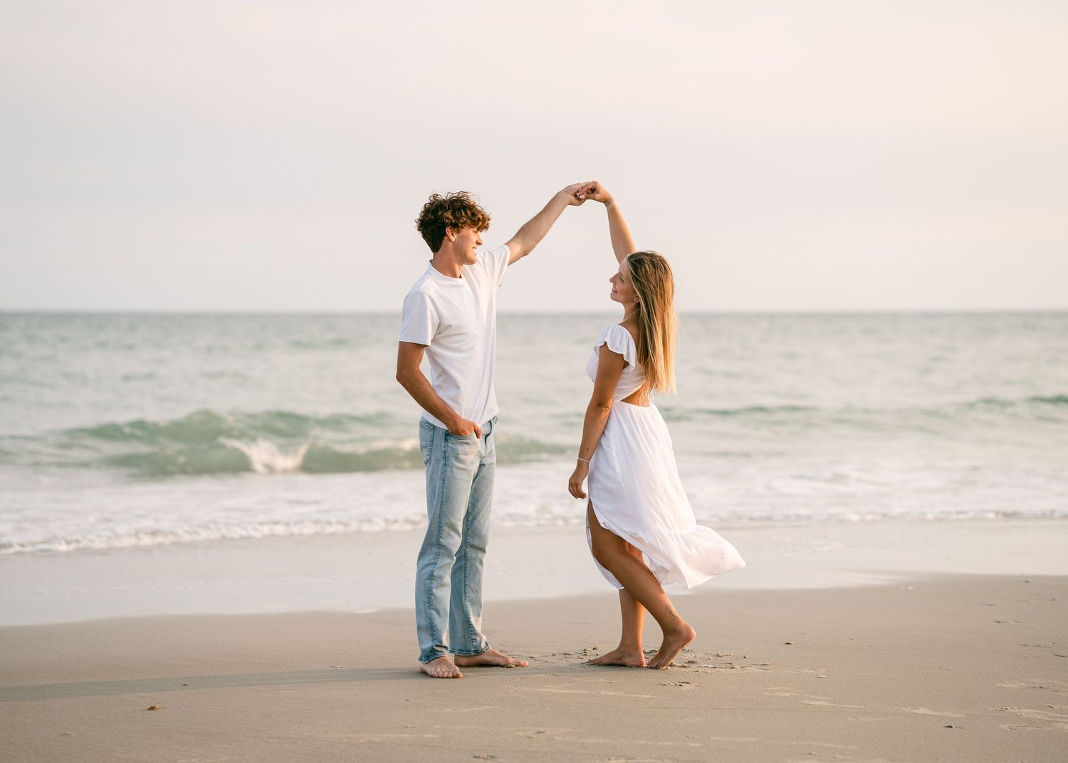 Couple dancing together on a sandy beach with ocean waves in the background.