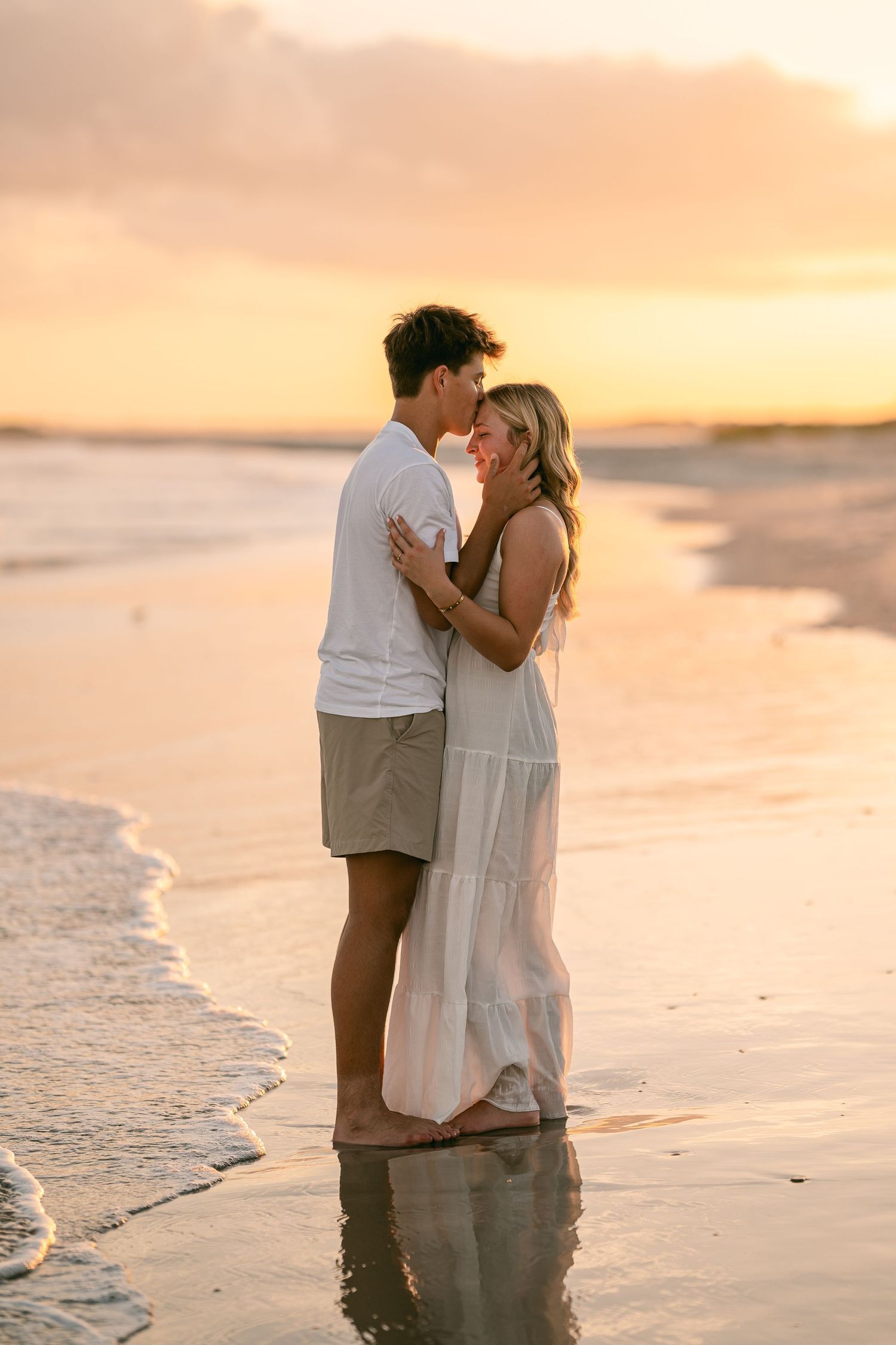 Couple sharing a tender moment on a sandy beach during a golden sunset by the ocean.