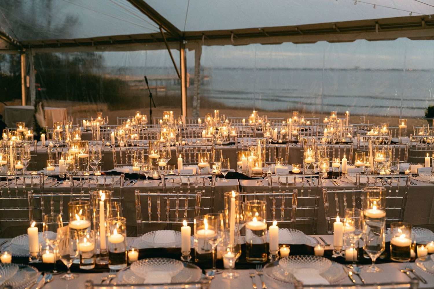 Elegant candlelit wedding reception under clear tent with glowing centerpieces overlooking a serene ocean view.