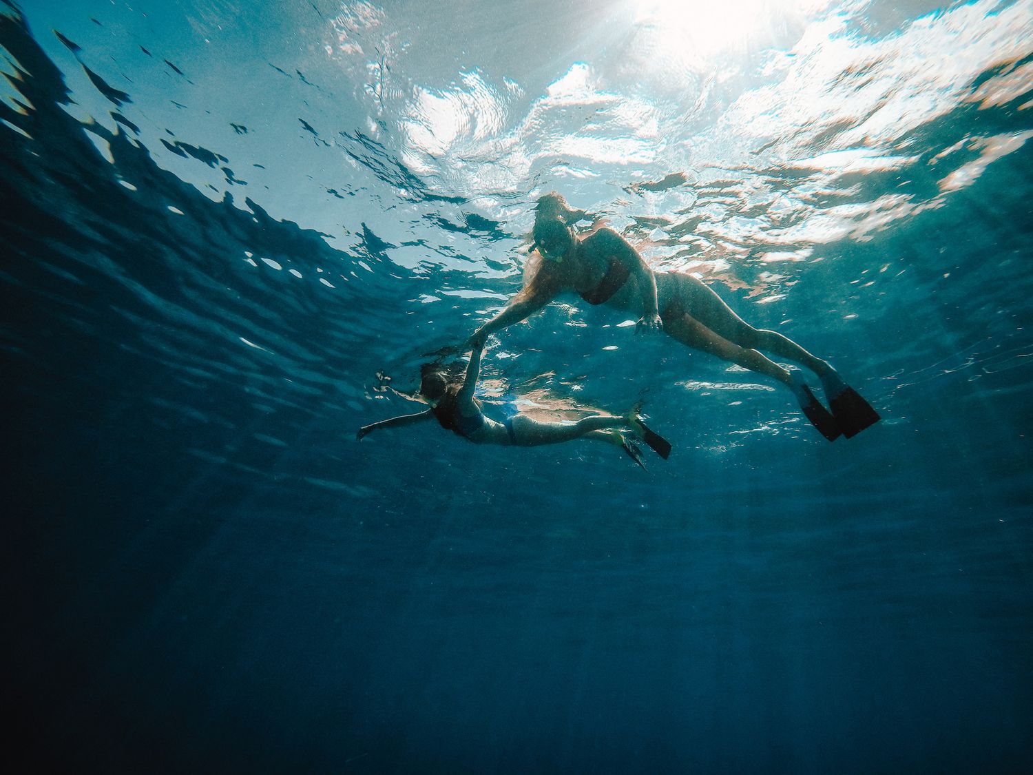 Two snorkelers swimming underwater in deep blue ocean with sunlight filtering from above.