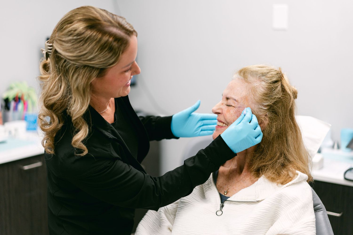 Female aesthetician in blue gloves examining patient face in medical spa.