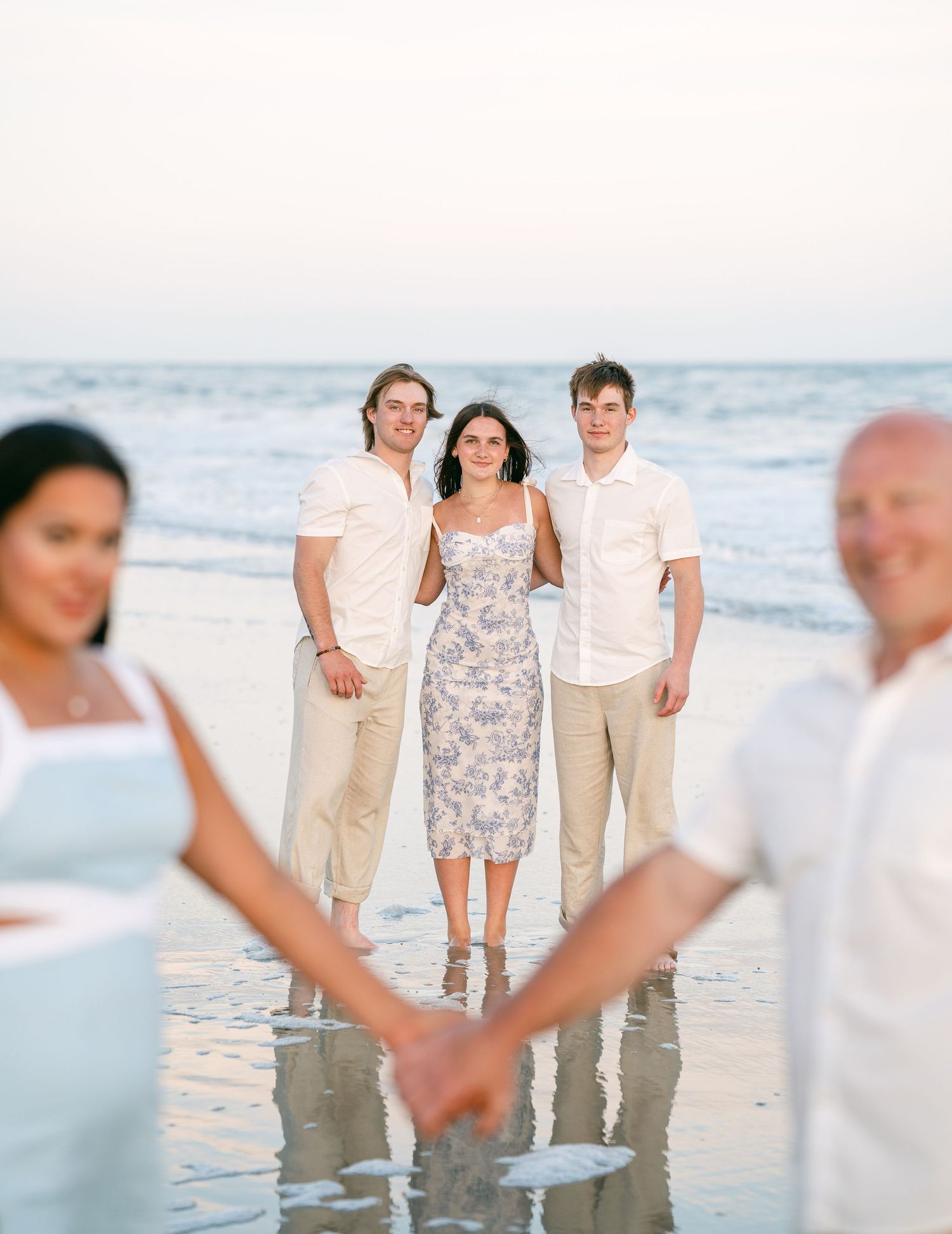 Three adult children standing in ocean surf while parents hold hands in foreground.