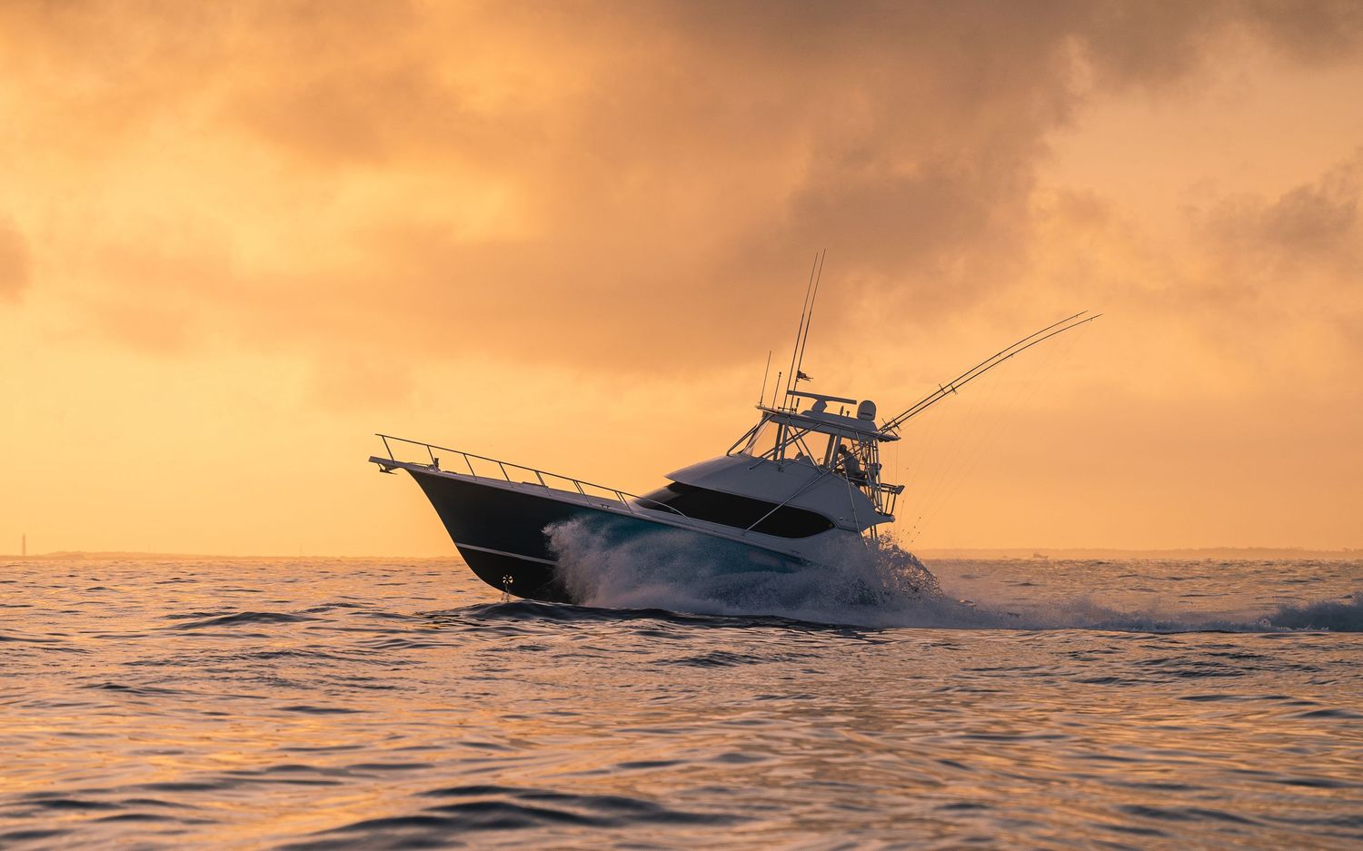 Sport fishing boat cruising across golden ocean waters beneath a vibrant sunset sky.