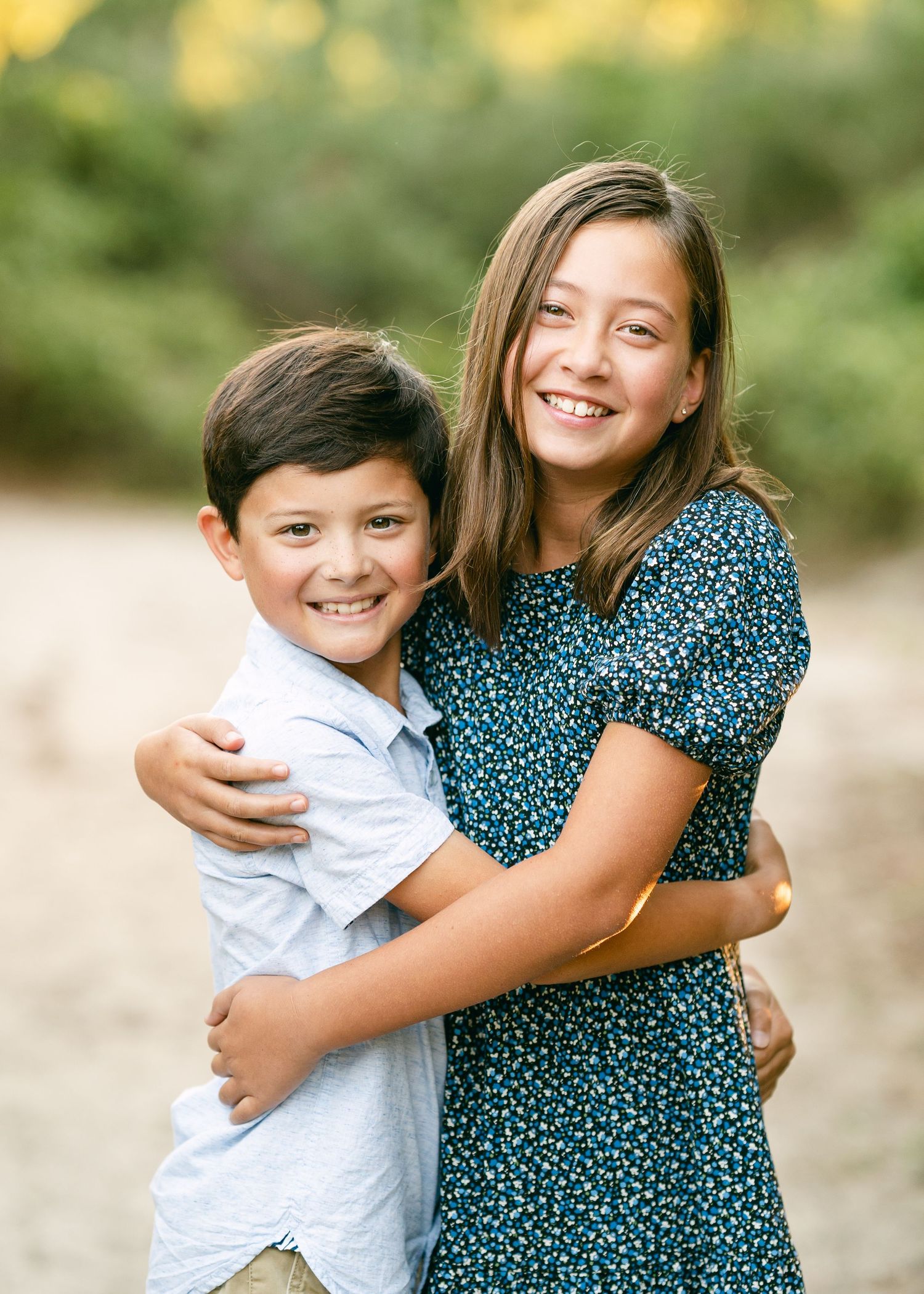 Young brother and sister hugging and smiling together on a sunny outdoor path.