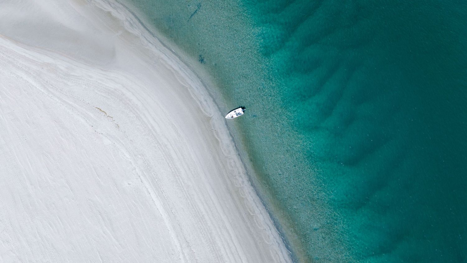 Aerial view of a small boat on a white sand beach with turquoise water.