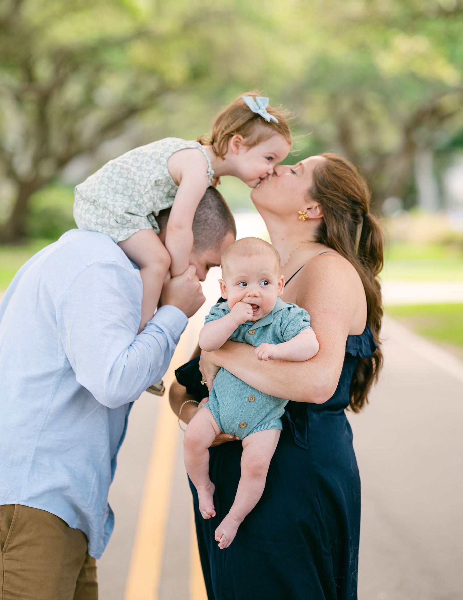 Loving family moment as parents kiss over baby and toddler on a scenic road.