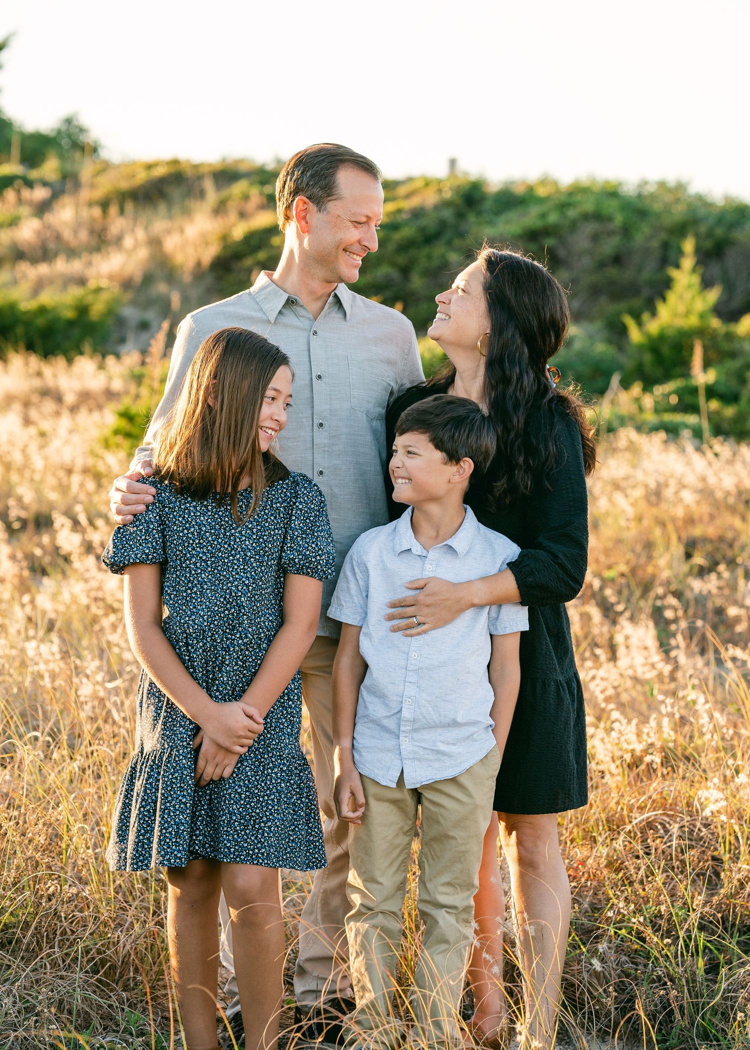 Happy family of four posing together in golden sunlit field during outdoor portrait session.