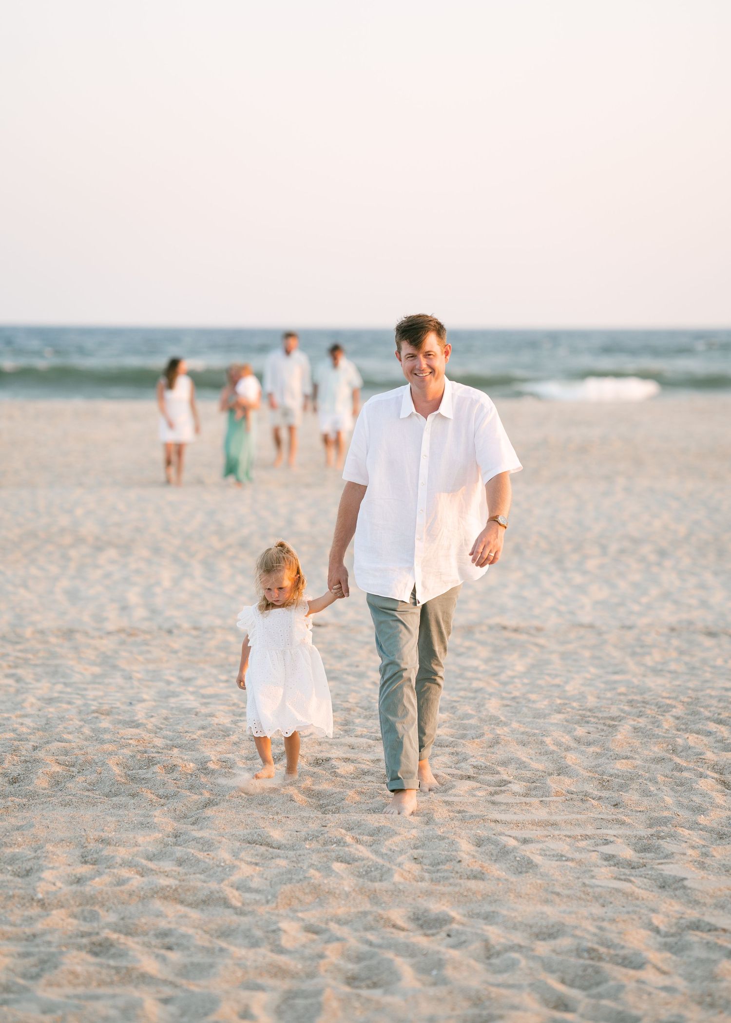 Father walking hand in hand with toddler daughter on a sunny beach.