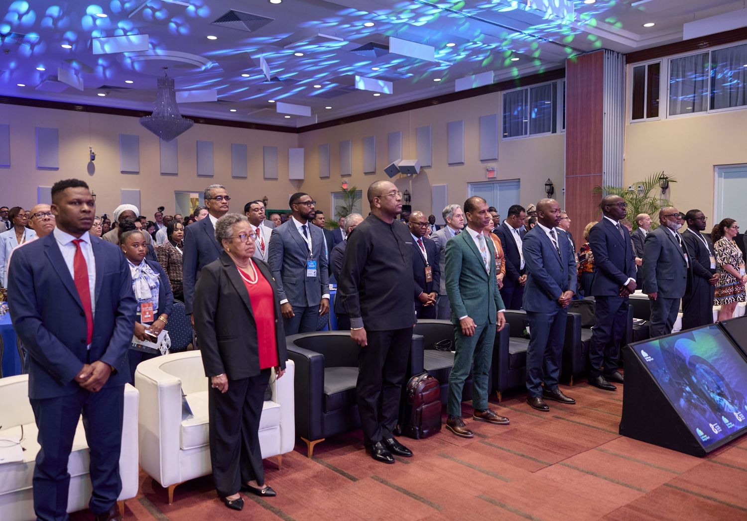 Attendees standing at attention during the opening ceremony of a formal international conference in a modern venue.