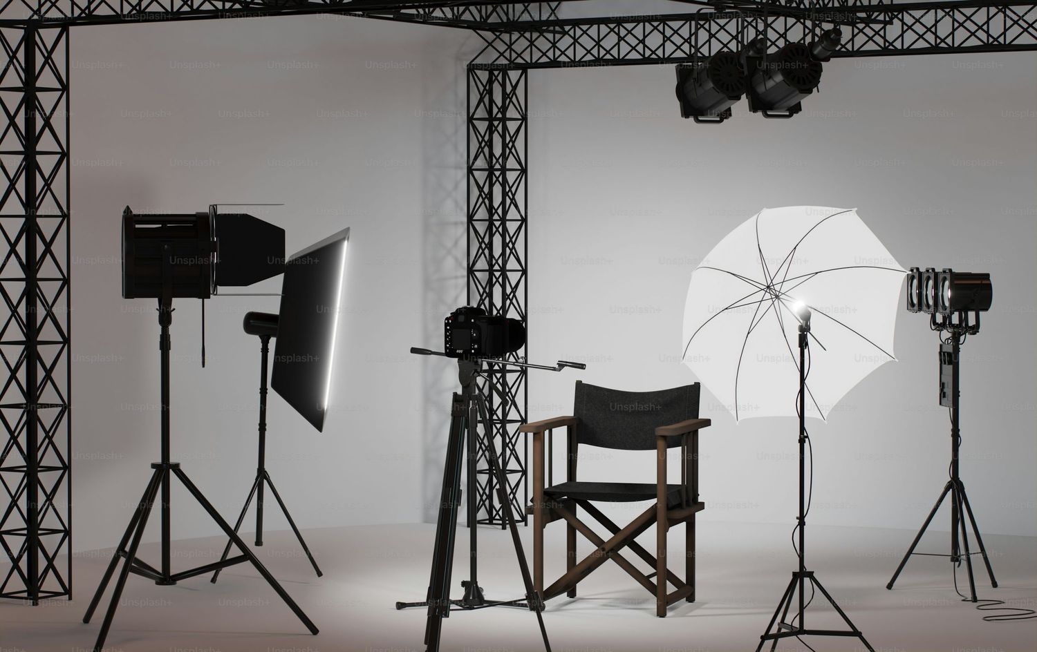 Professional photography studio setup with lighting equipment, white backdrop, director chairs and umbrella reflectors.