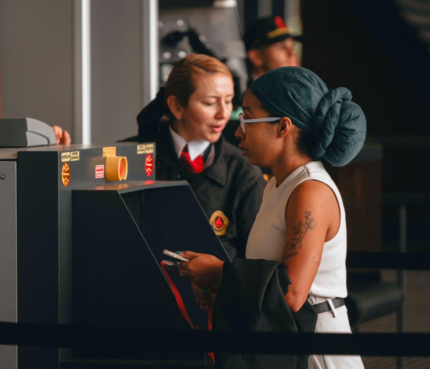 Woman with gray head wrap checking in at airport security kiosk with staff.