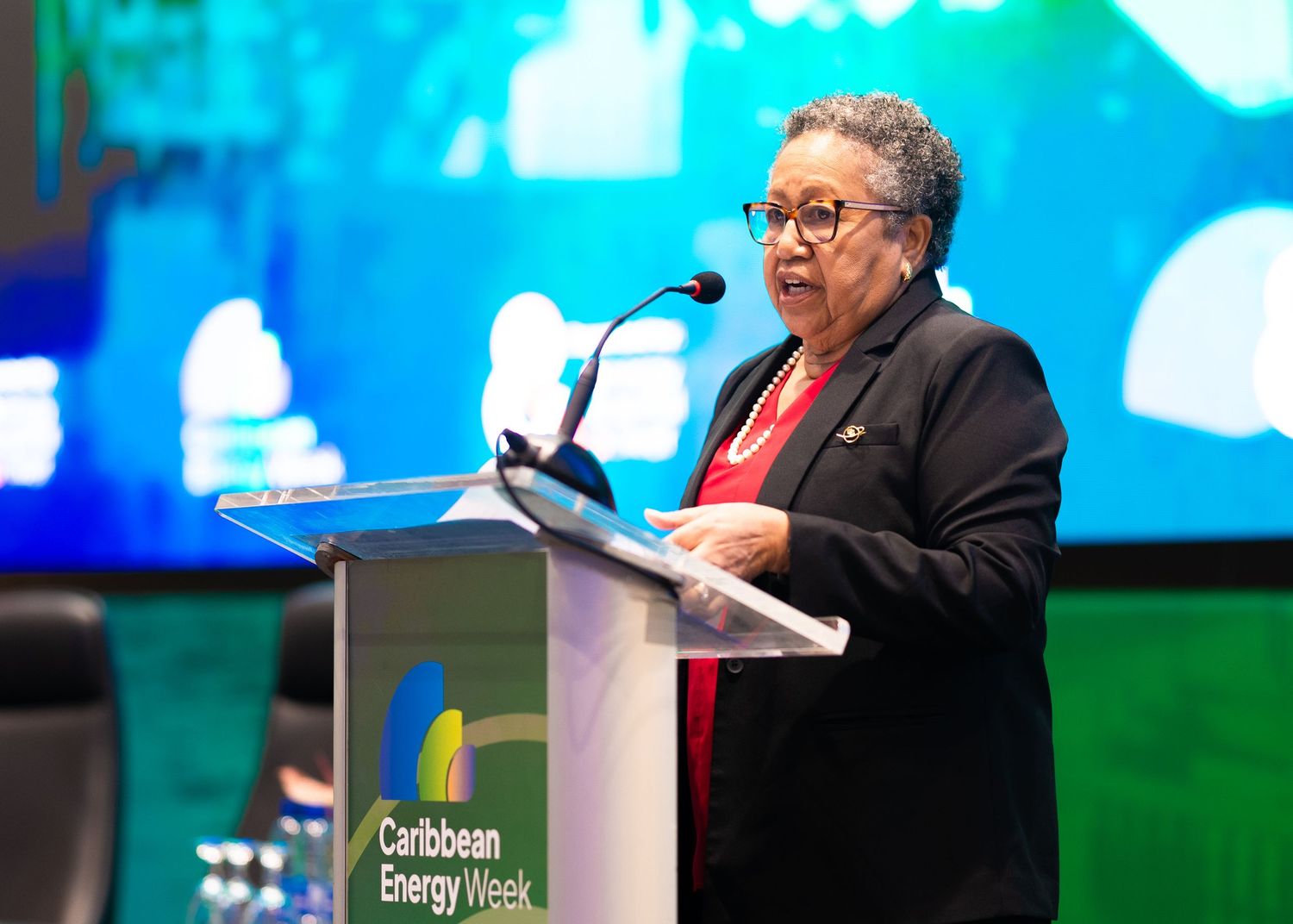 Woman speaking at podium during Caribbean Energy Week conference event.