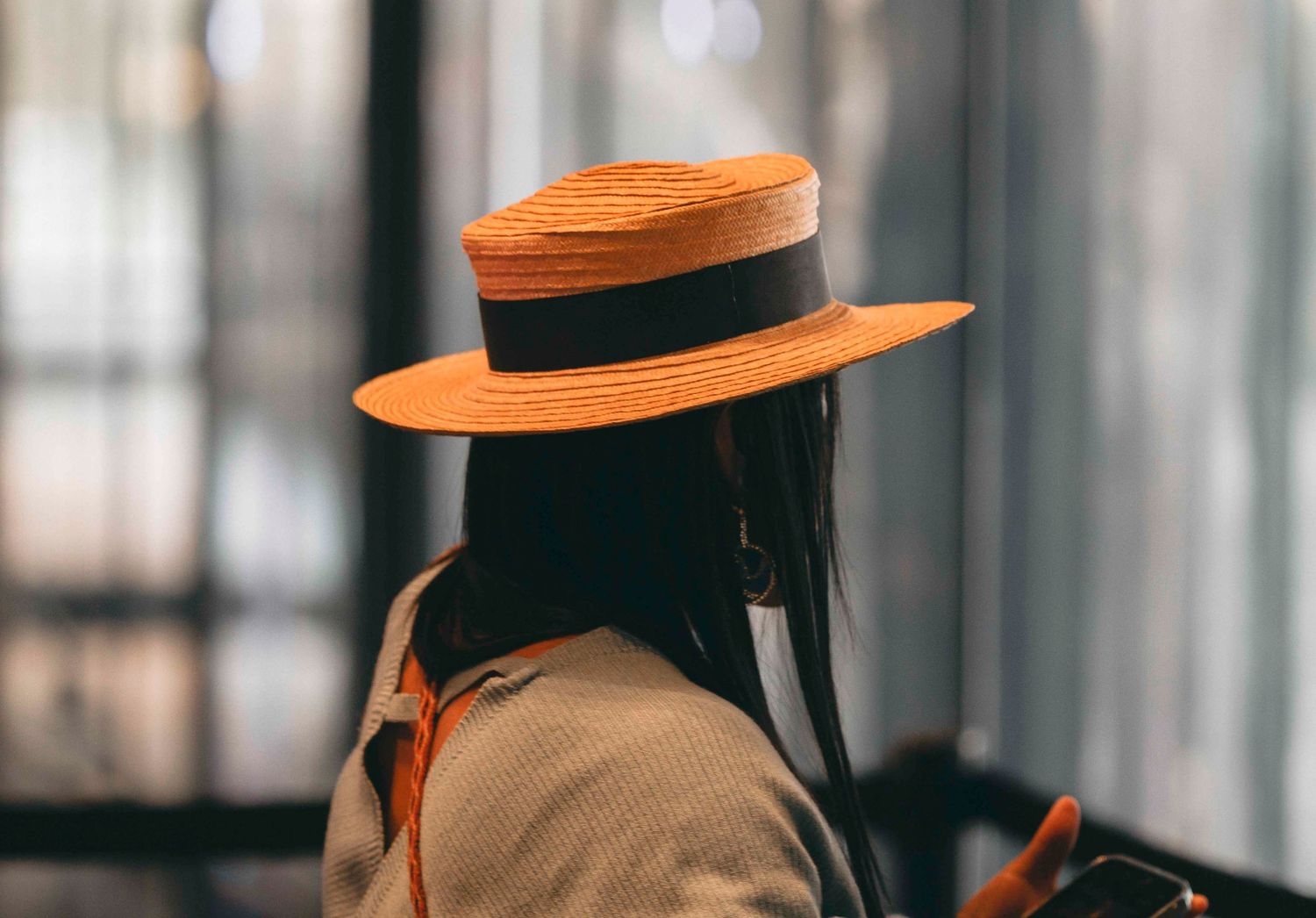 Woman wearing a stylish orange straw hat with black ribbon band outdoors.