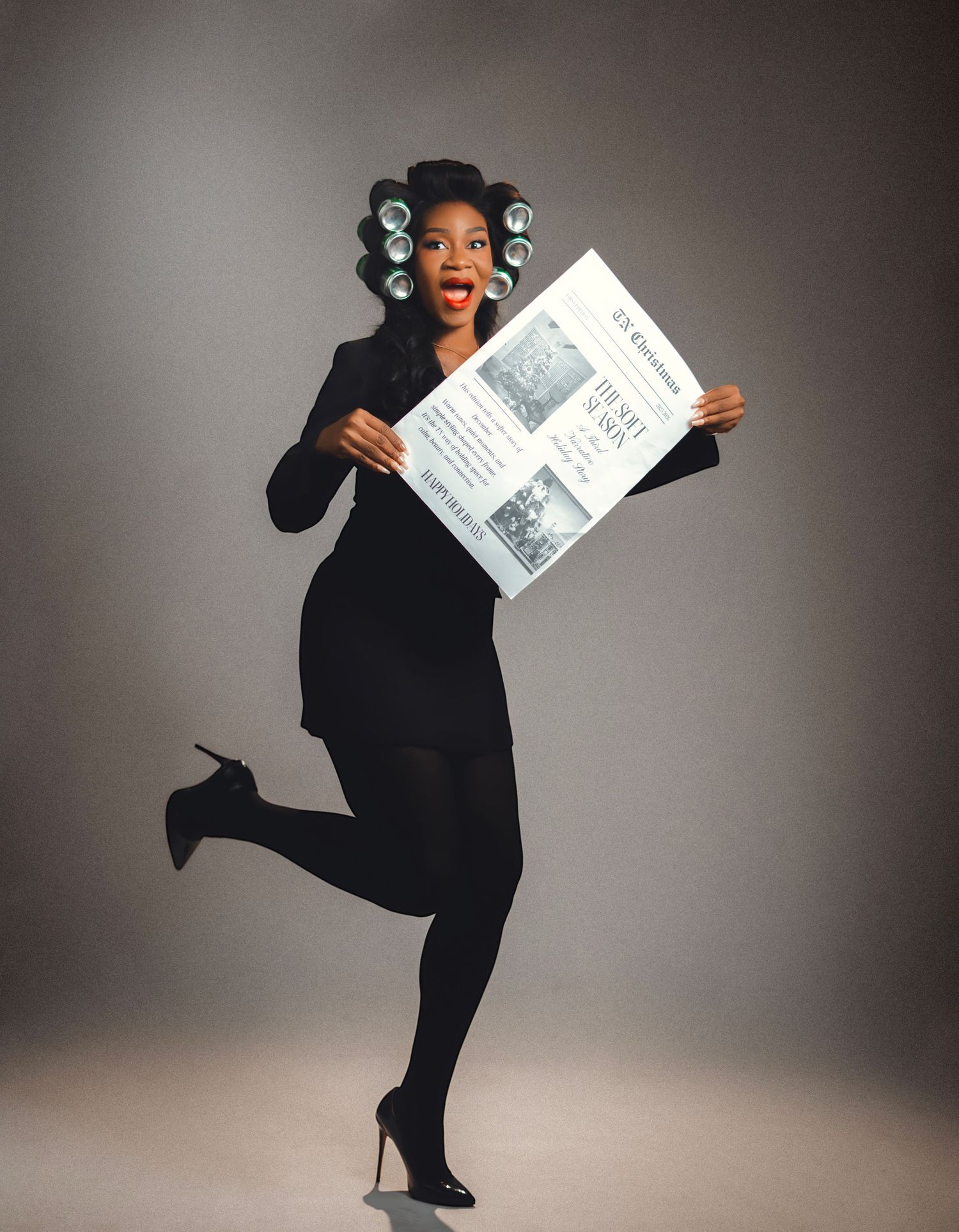 Energetic figure in black dress and hair rollers jumps excitedly while holding up a newspaper against gray backdrop.