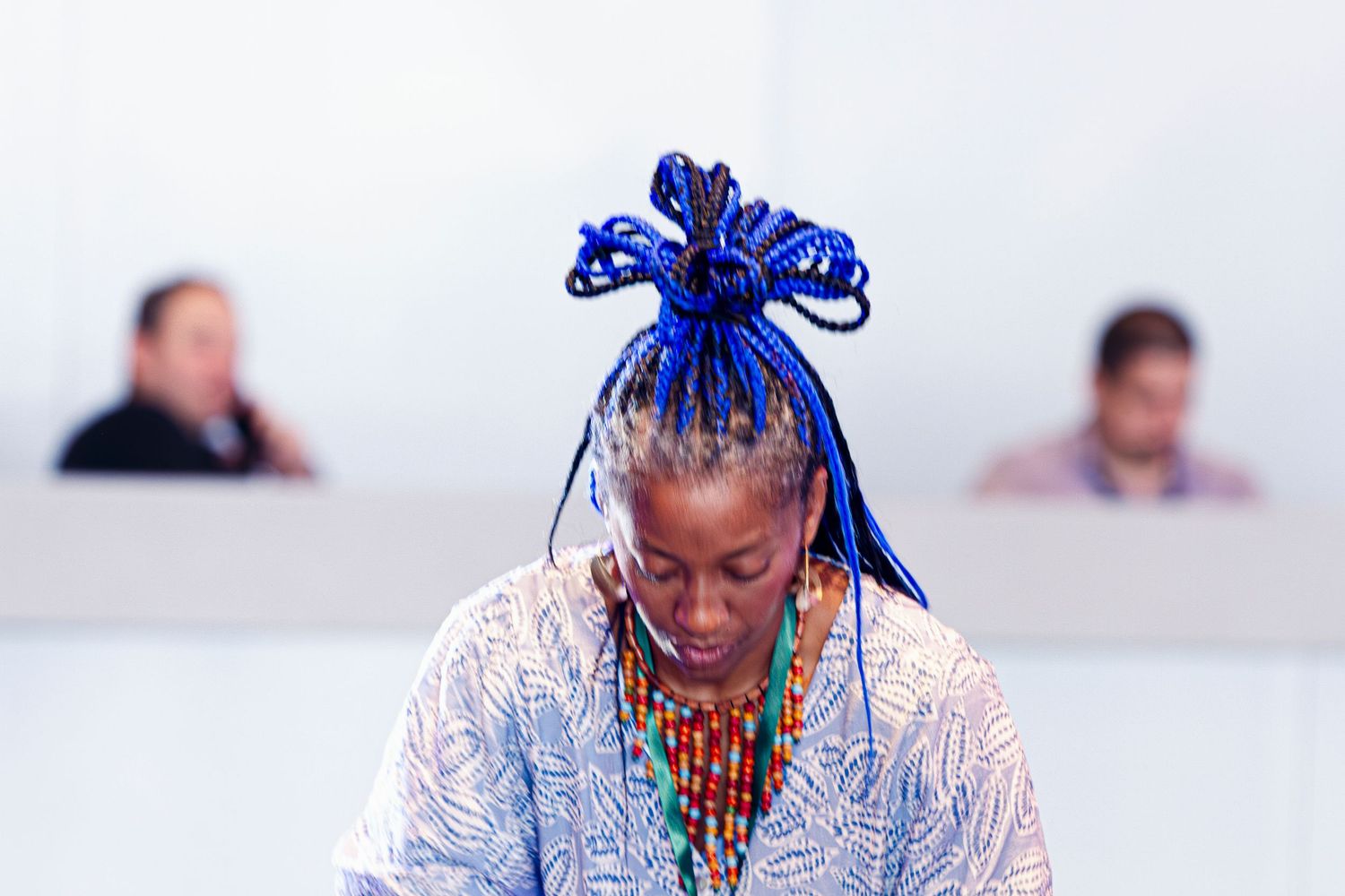 Woman with vibrant blue braided hair and colorful beaded necklace at an event.