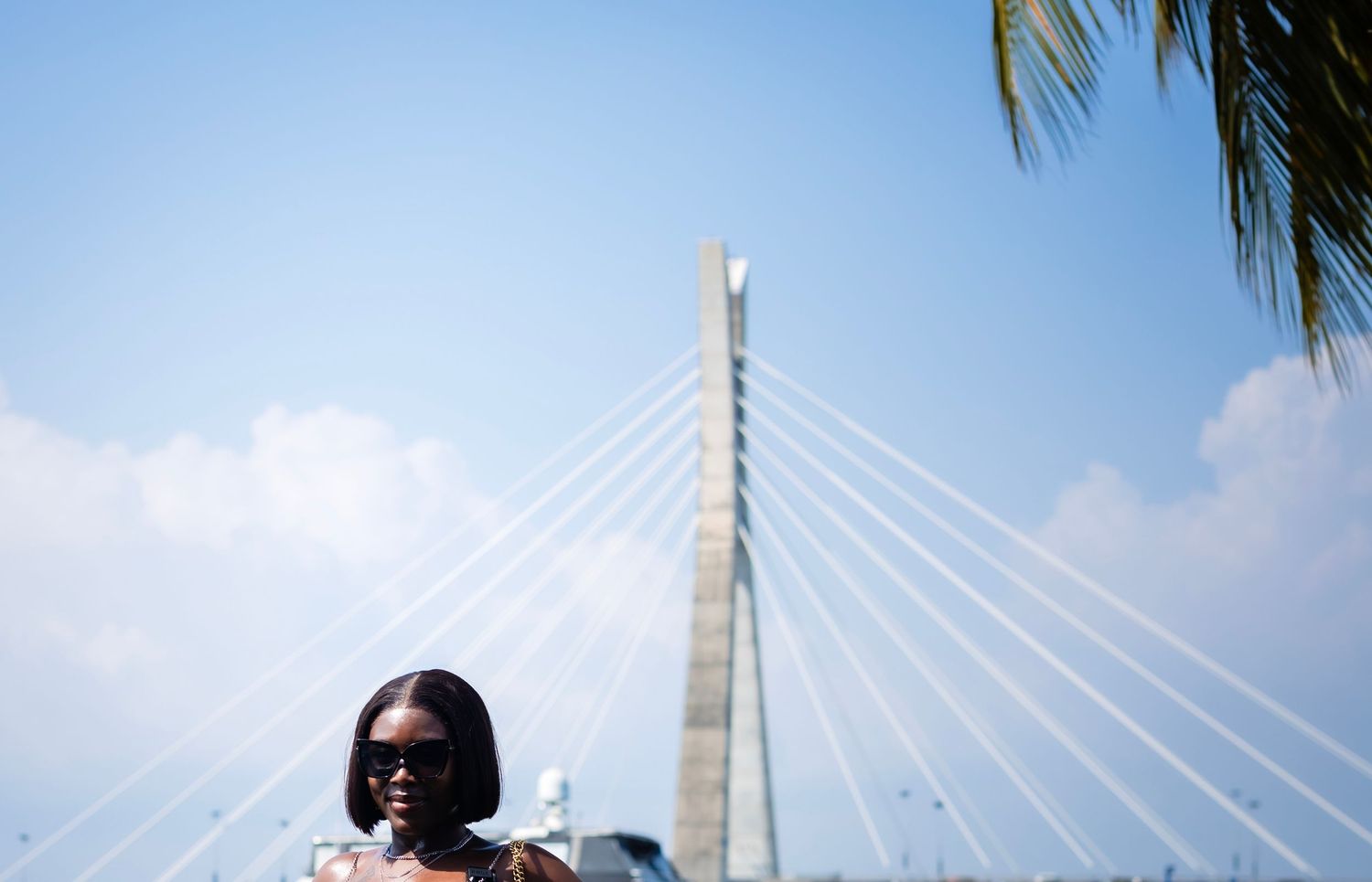 People enjoy scenic views from a waterfront walkway near a modern cable-stayed bridge on a sunny day.