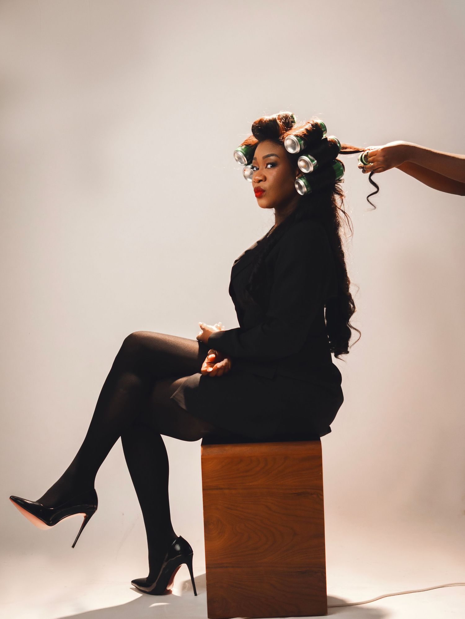 A stylish figure in black attire strikes dynamic poses while seated on a wooden cube against a neutral backdrop.