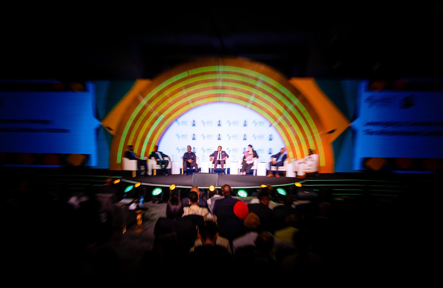 Stage with rainbow-colored arch illuminated in dark auditorium during performance.