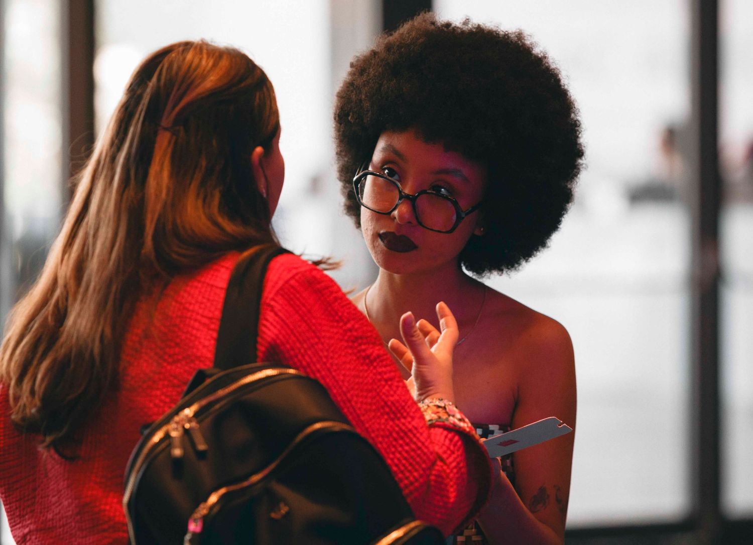 Two women in red outfits having a conversation, one with an afro and glasses, the other with long red hair.