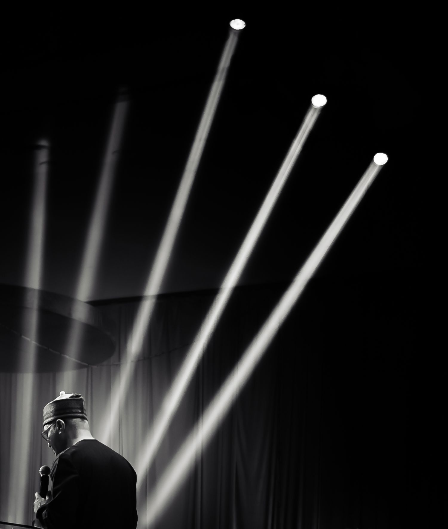 Dramatic black and white stage performance with silhouetted figure against striking beams of bright spotlights.
