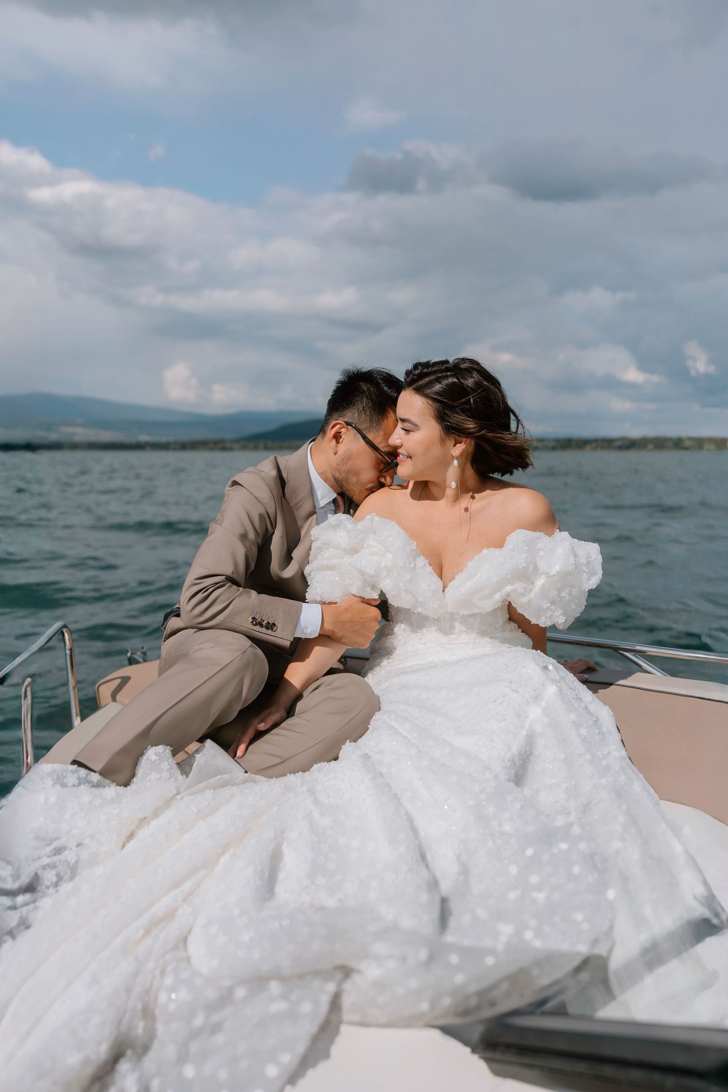 Wedding couple sharing intimate moment on boat with scenic lake view.
