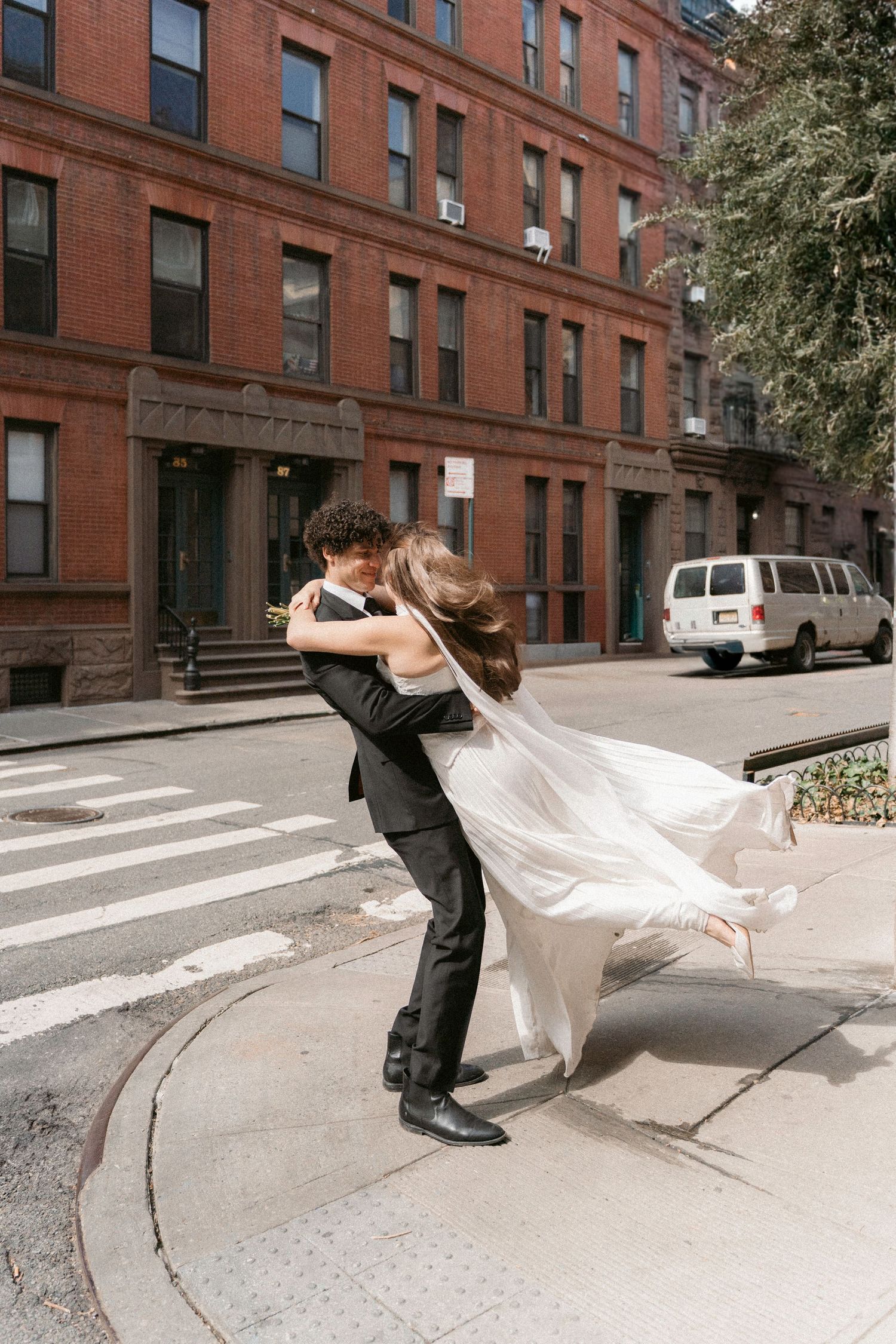 Couple performing dramatic dip kiss on urban street with brick buildings.