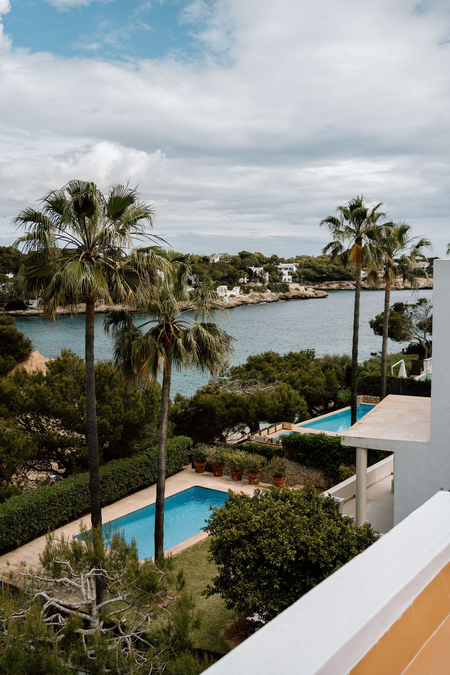 Seaside resort view with palm trees, swimming pool, and Mediterranean coastline.