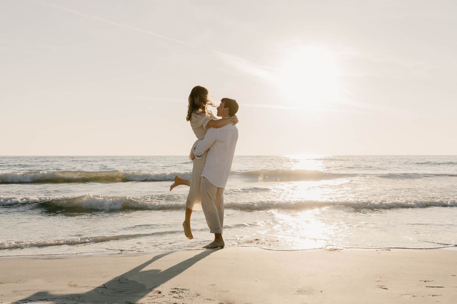 Romantic sunset beach wedding portrait with couple silhouetted against ocean waves.