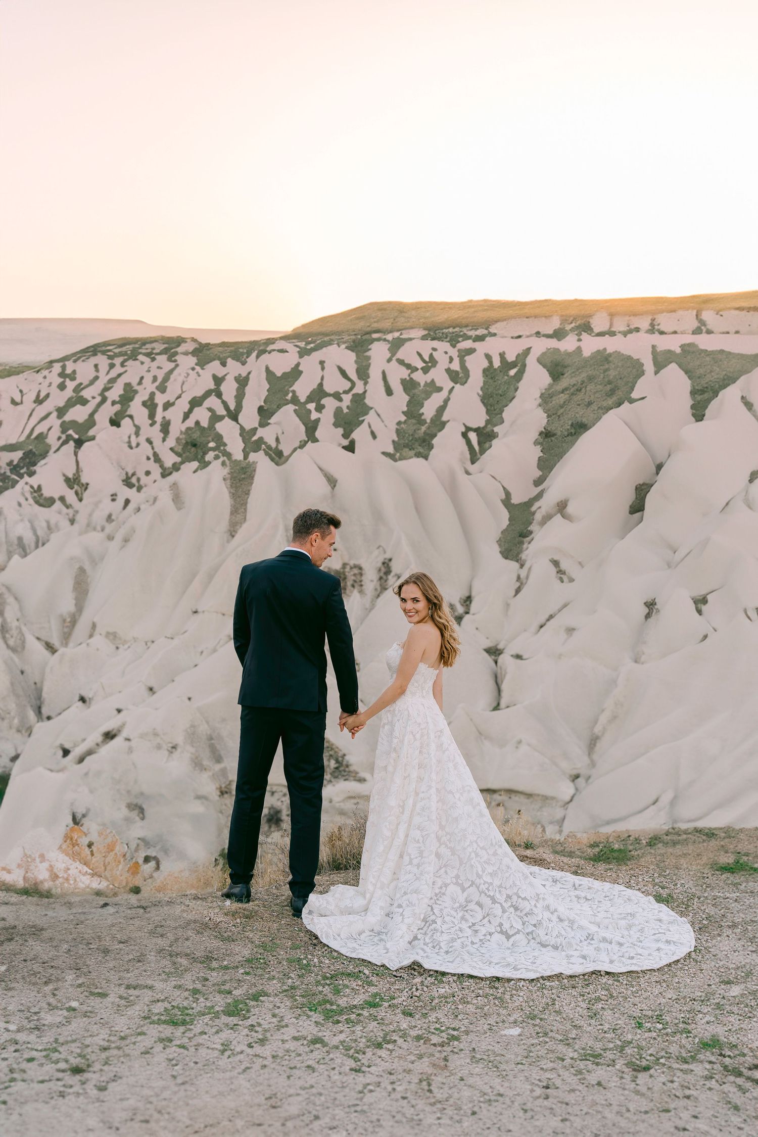 Bride and groom pose against white rock formations during sunset for wedding photos.