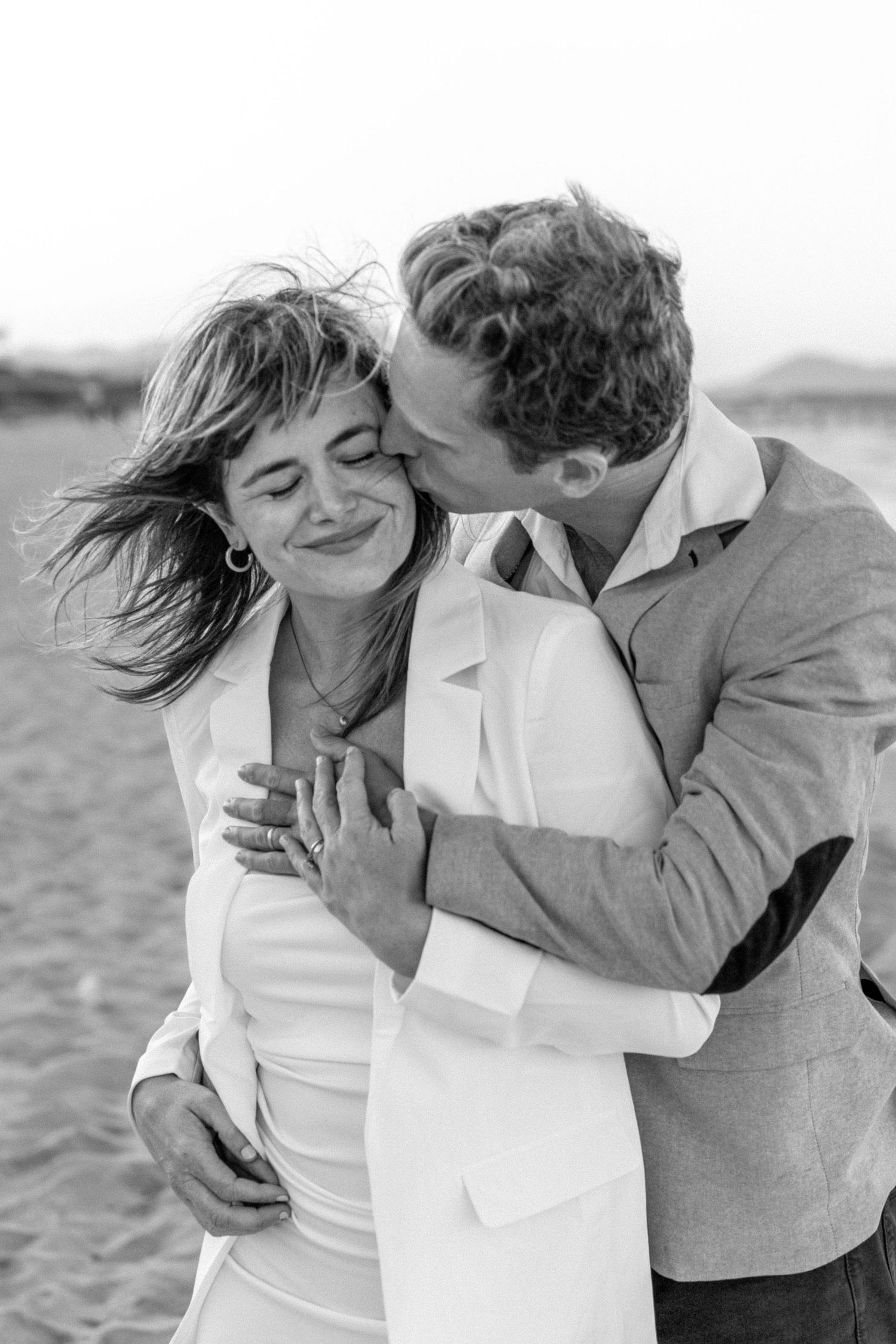 A romantic black and white photo sequence showing a couple embracing on a beach with windswept hair.