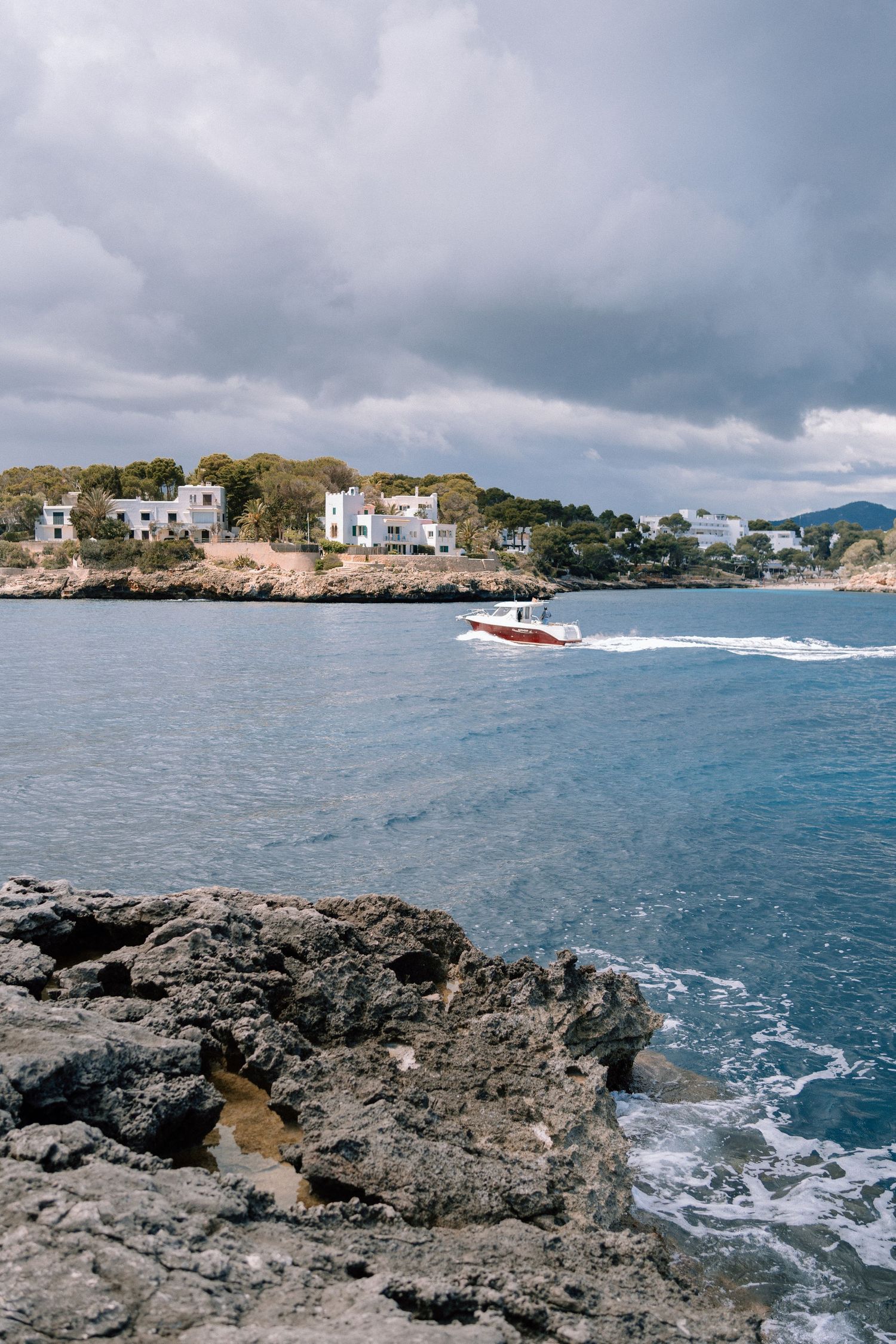 Rocky coastal landscape with turquoise waters and distant buildings under cloudy skies.