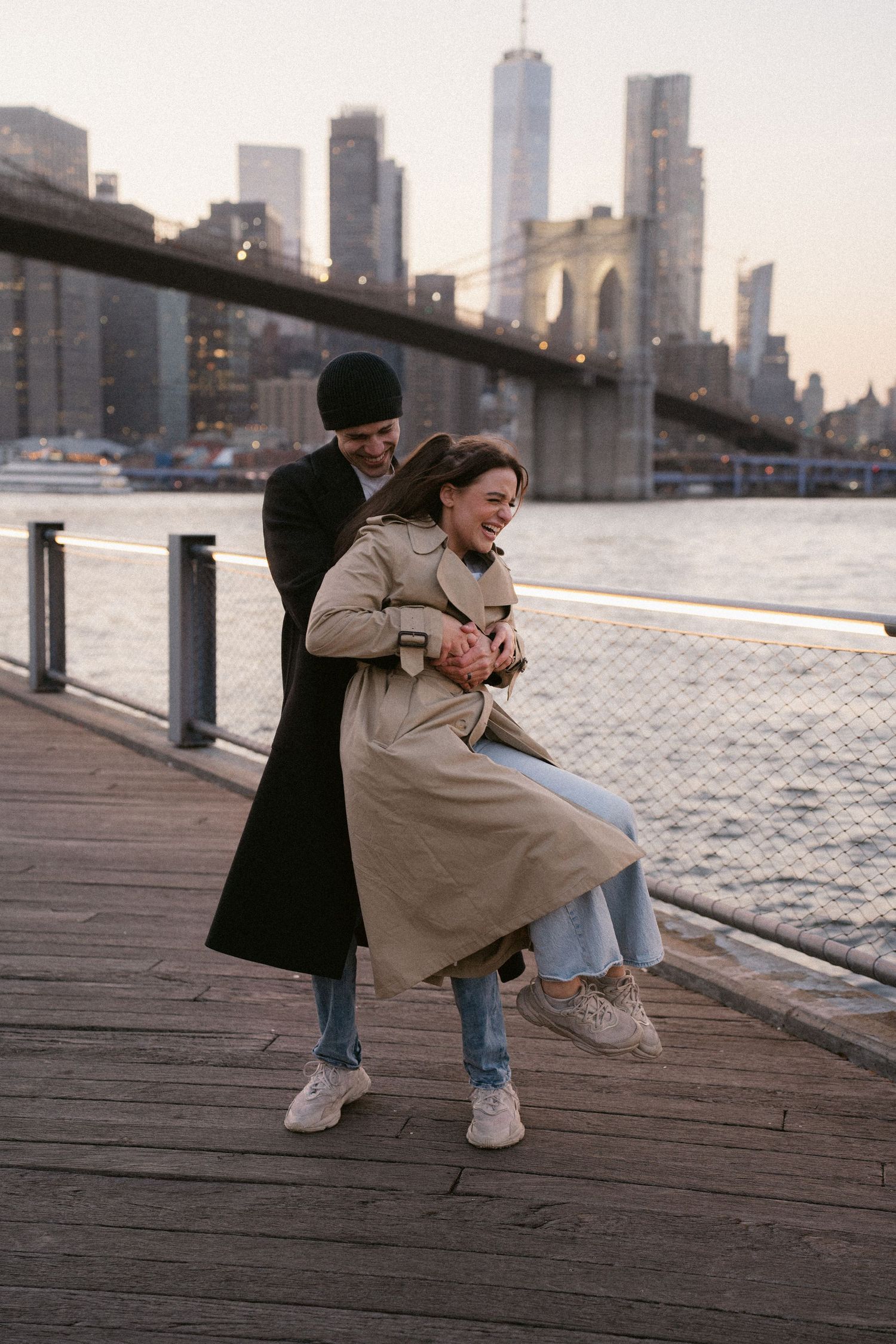 Two figures crouching on wooden pier with urban skyline backdrop.