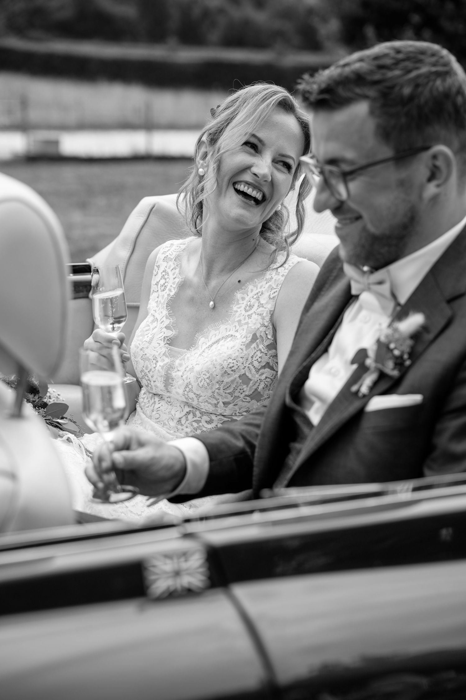 A joyful couple laughing together in a classic car on their wedding day.