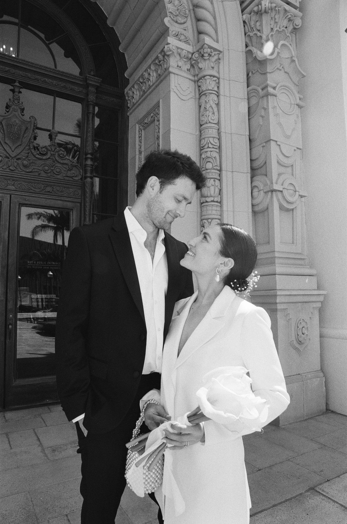 Romantic couple in formal attire embracing beneath ornate architectural columns.