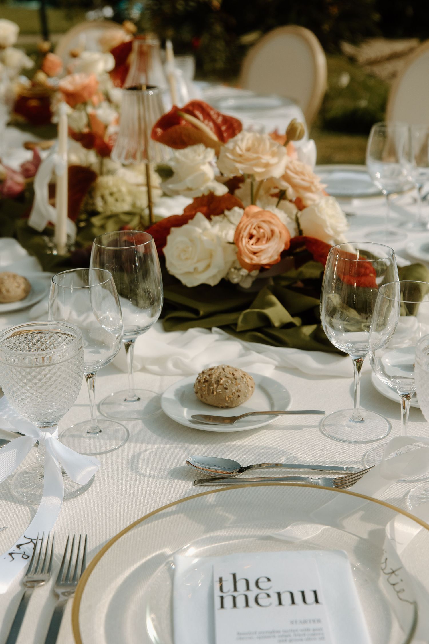 Luxurious wedding table settings with white plates, crystal glasses, and coral floral arrangements.