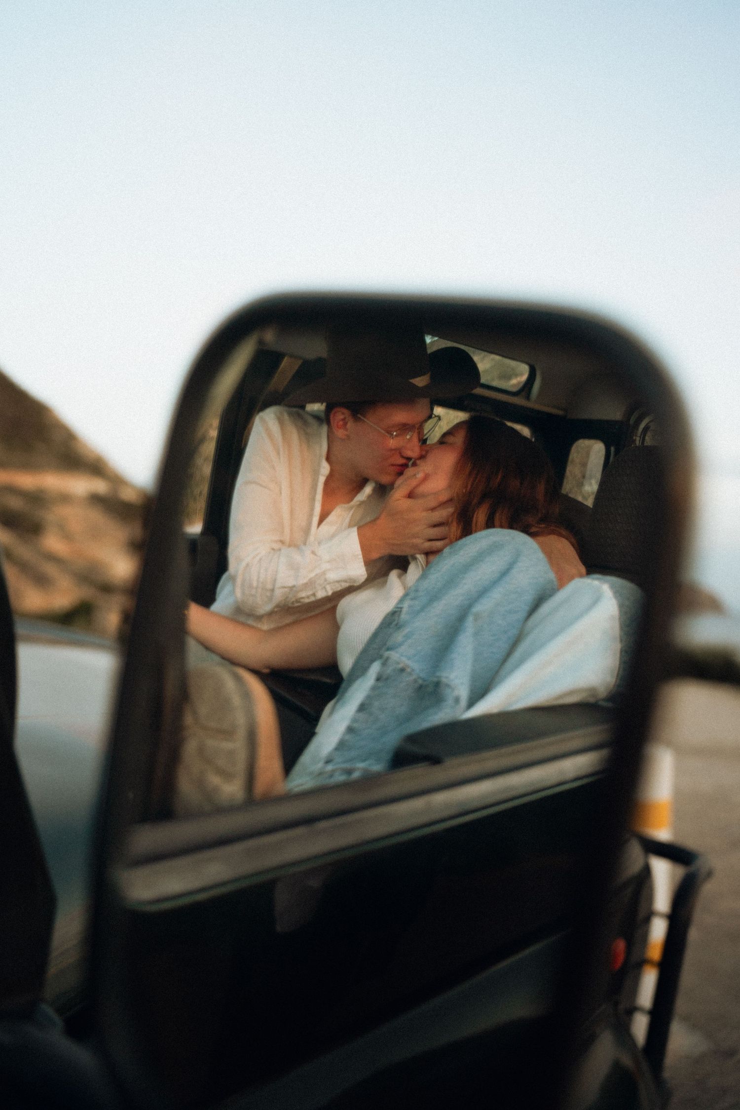 A romantic moment captured through a car window showing a couple sharing an intimate kiss.