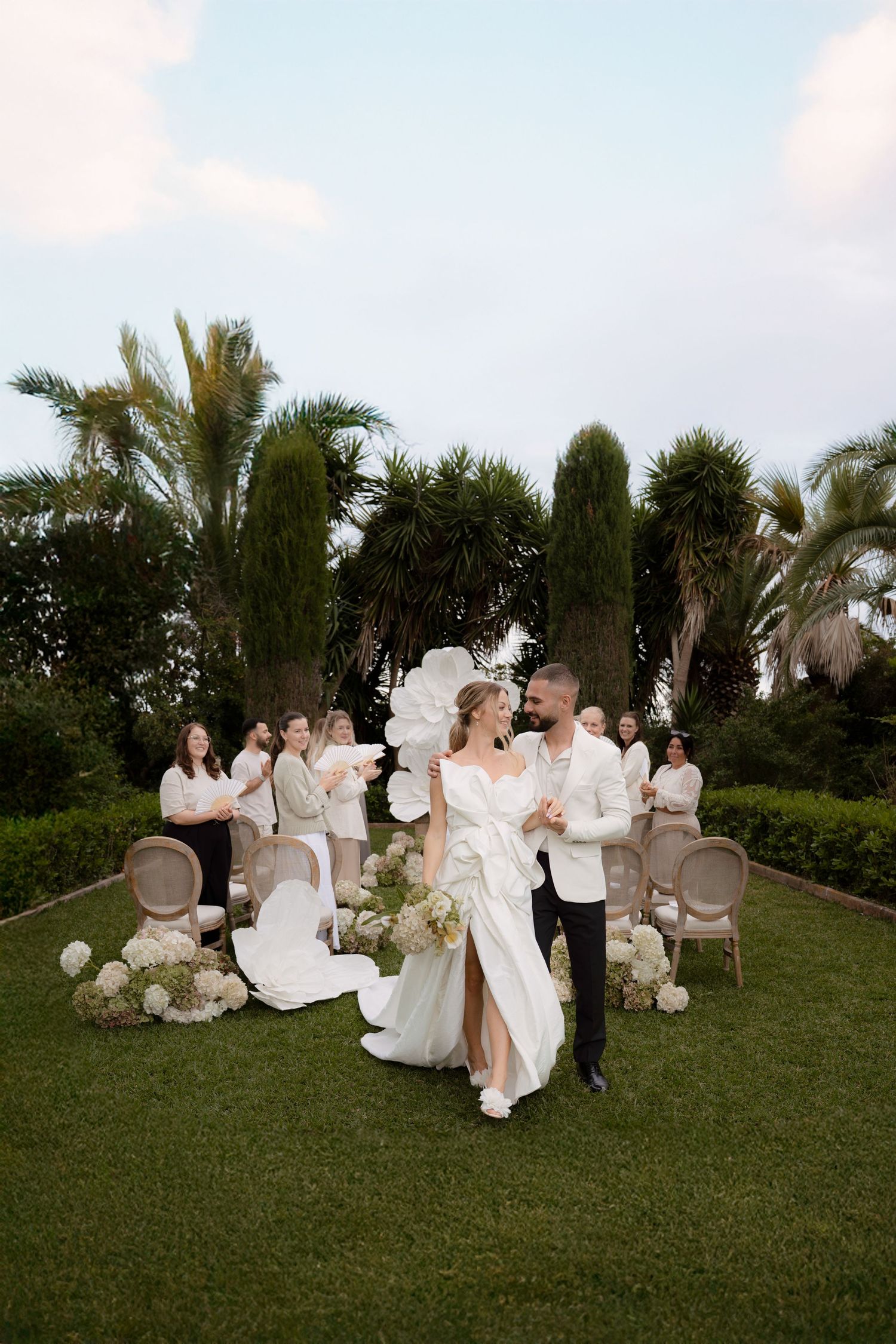 Elegant outdoor wedding ceremony setup with white chairs and decorations on a grassy lawn.