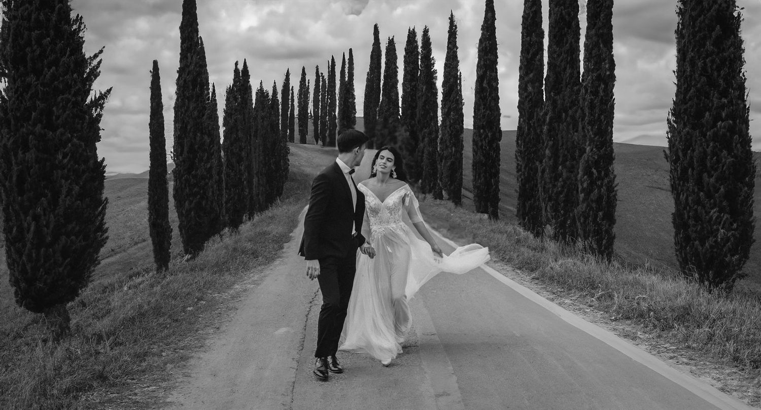 Dramatic wedding photo composition framed by tall cypress trees in black and white.