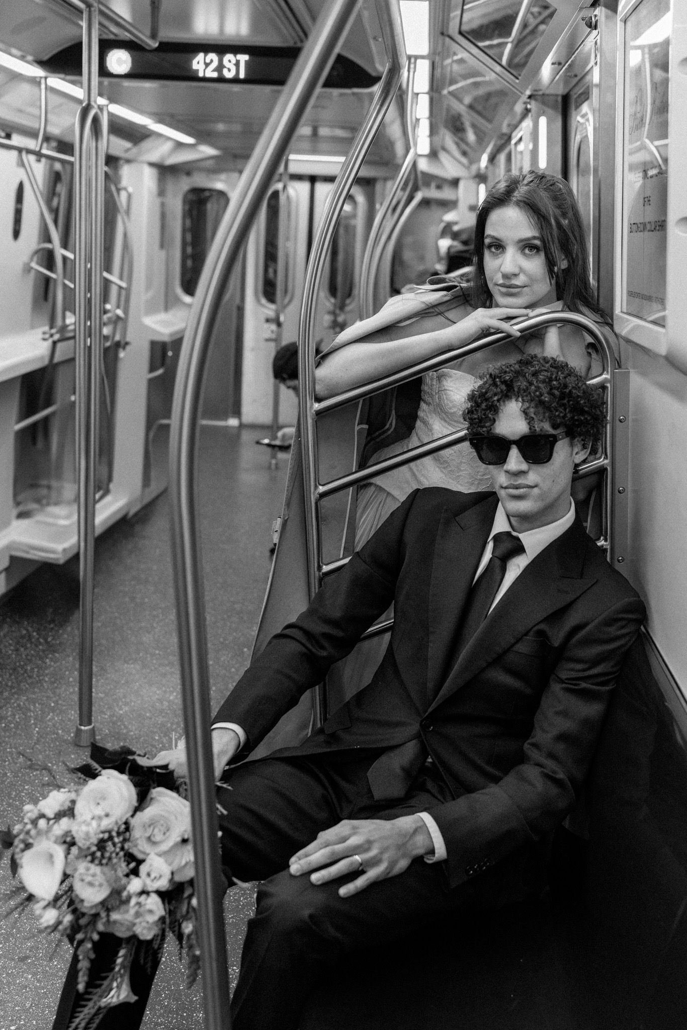 A black and white photo of newlyweds sitting together on subway train.