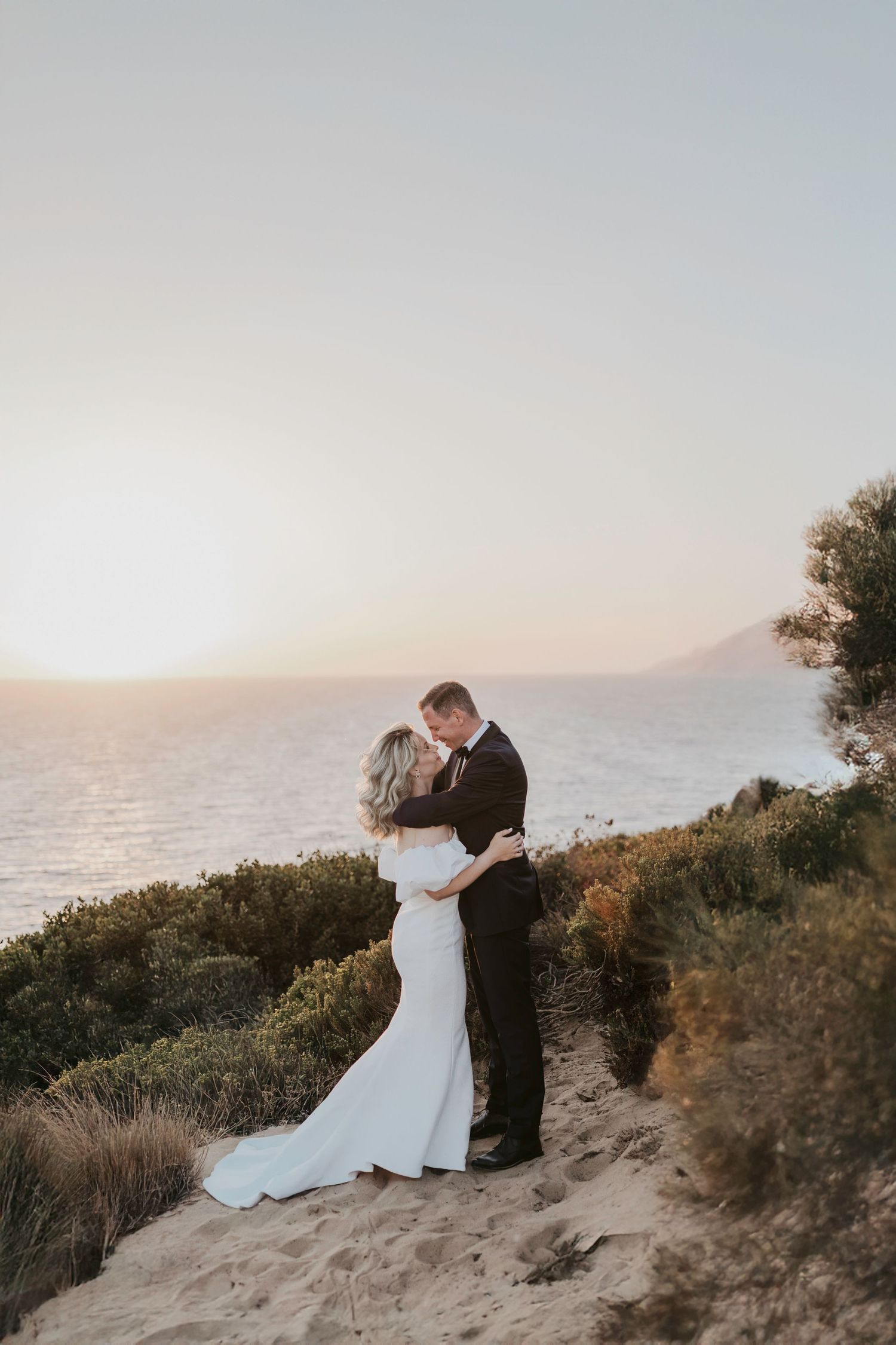 Romantic sunset wedding photos captured against a coastal cliff backdrop.