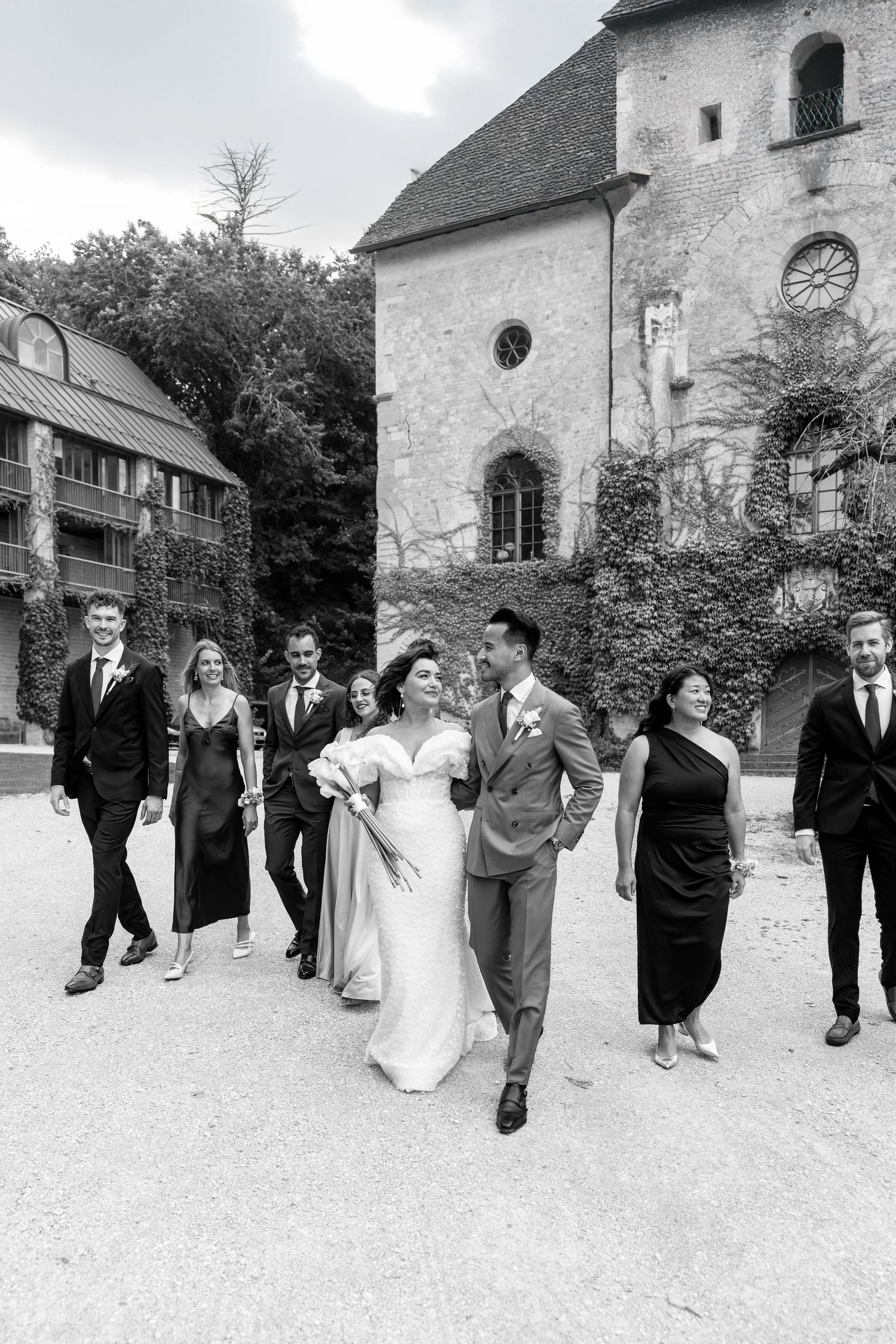 Wedding party walks together in black and white along stone church pathway.
