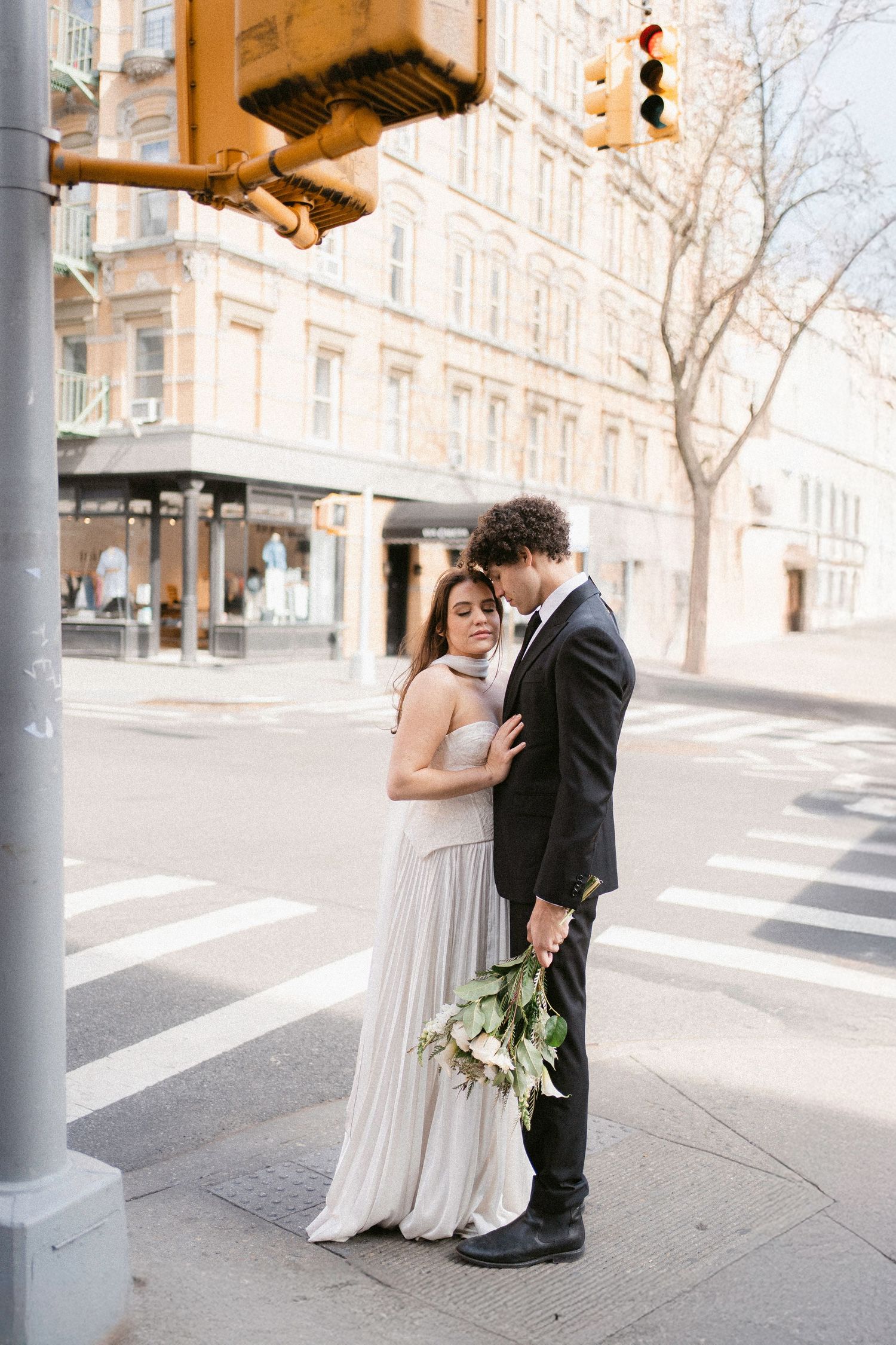 A couple shares romantic moments near street poles in an urban setting.