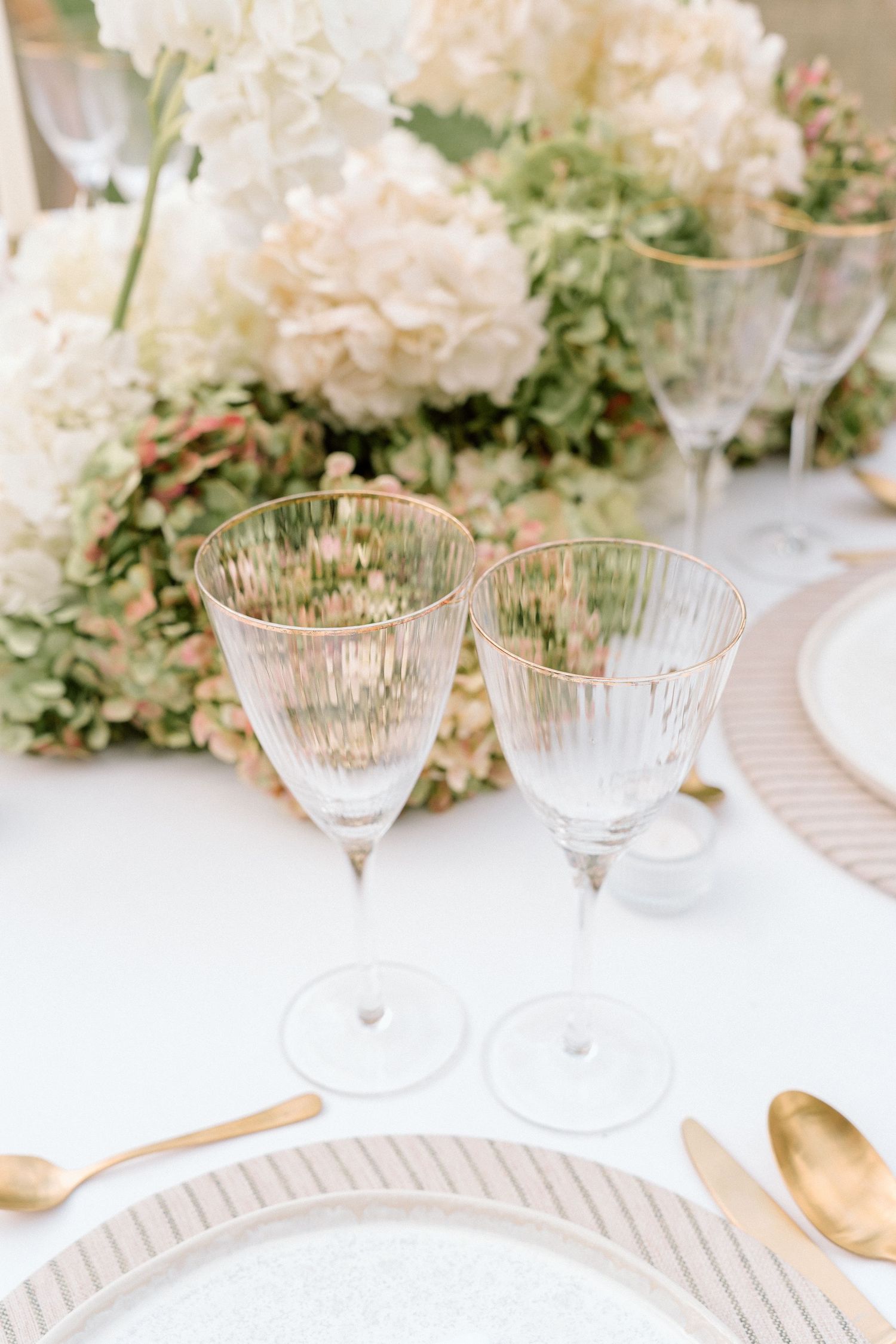 Crystal glassware and place settings on a white tablecloth with delicate floral arrangements.