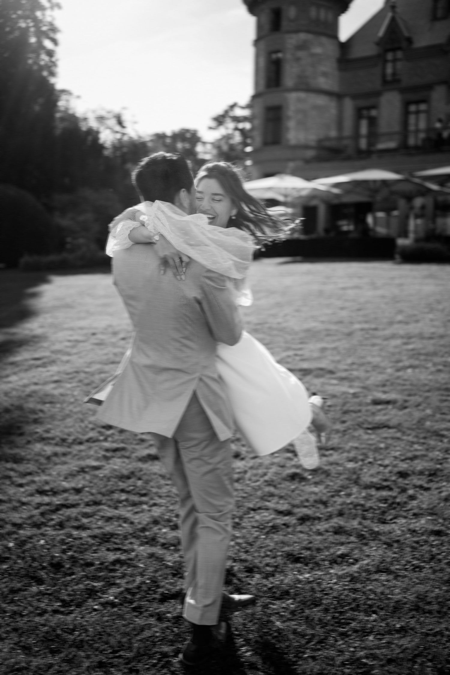 Black and white image of a couple dancing joyfully on a castle lawn.