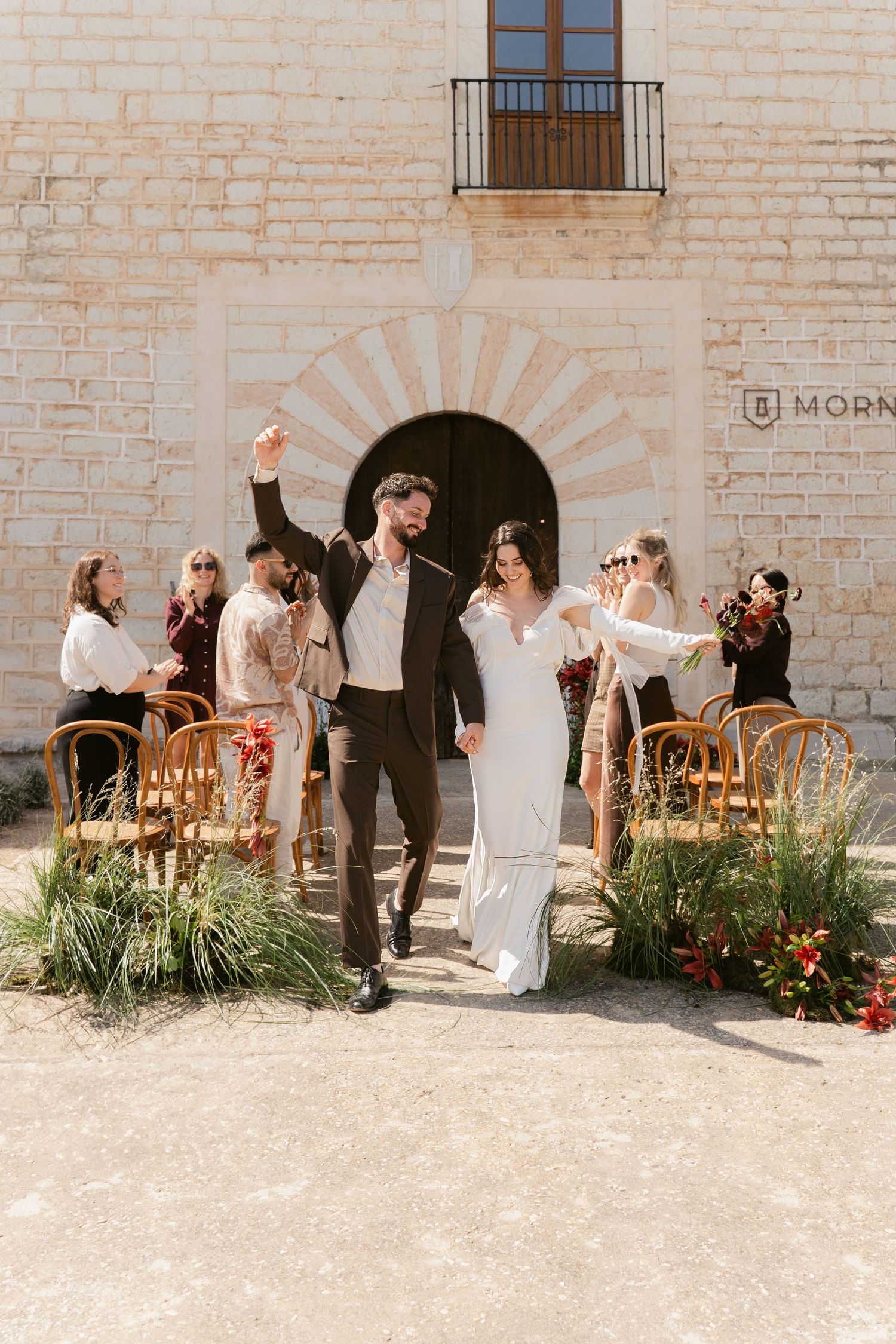 Wedding celebration outside a rustic stone building with elegant architectural details.