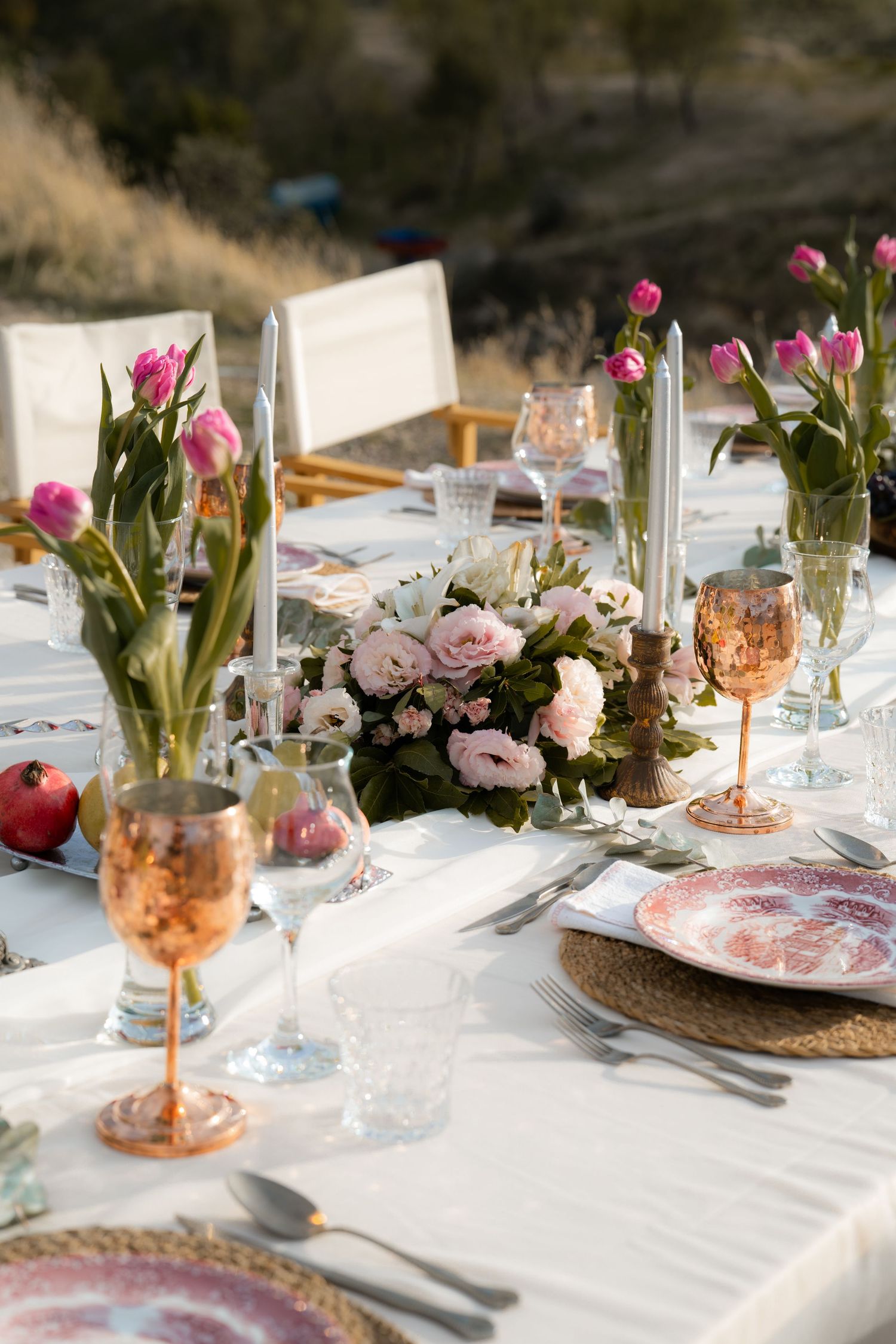 Elegant outdoor table set with pink roses, tulips, copper goblets, floral plates and white candles for a romantic al fresco wedding.