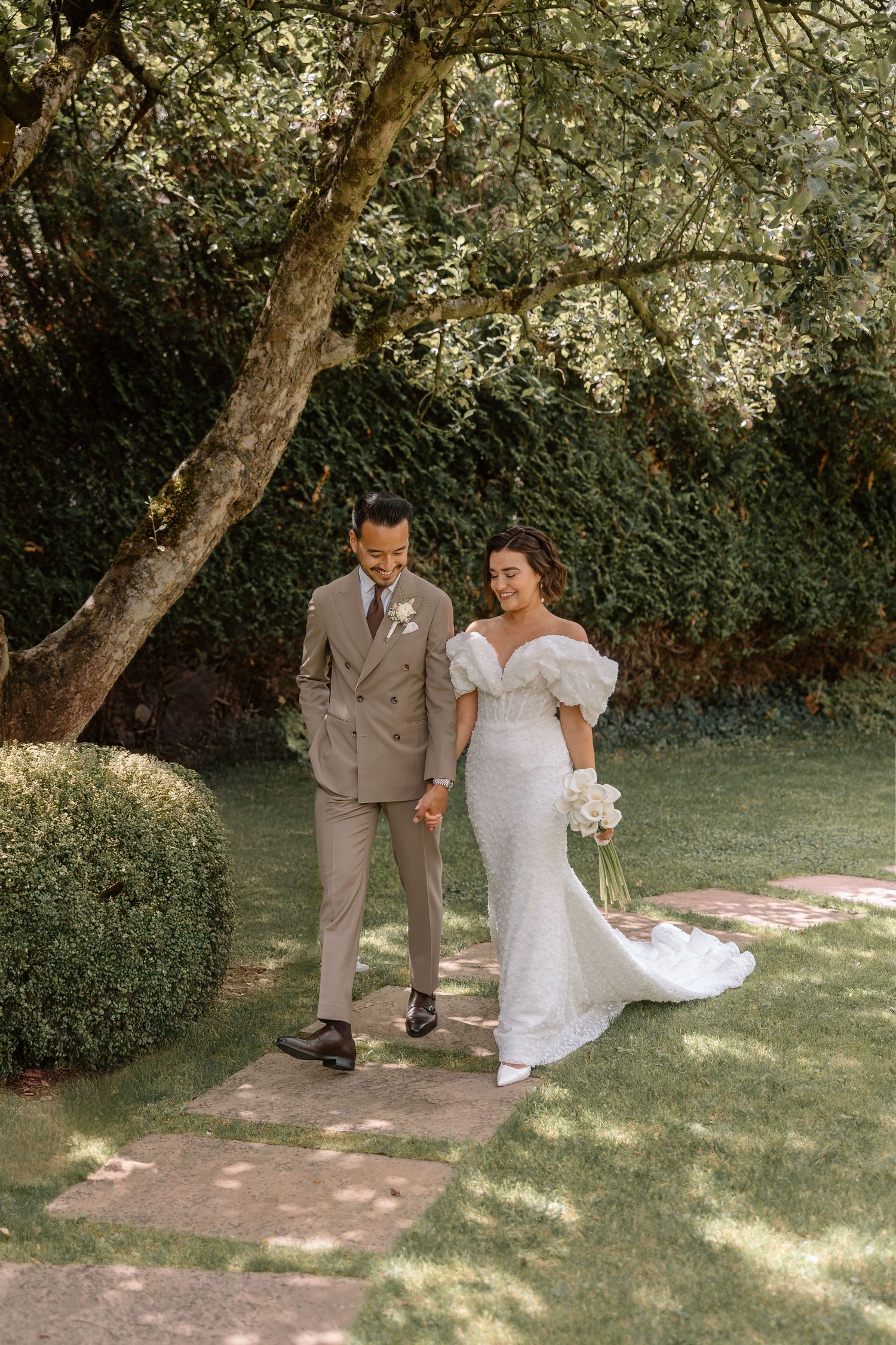 Couple walking together beneath blooming trees in a garden setting.