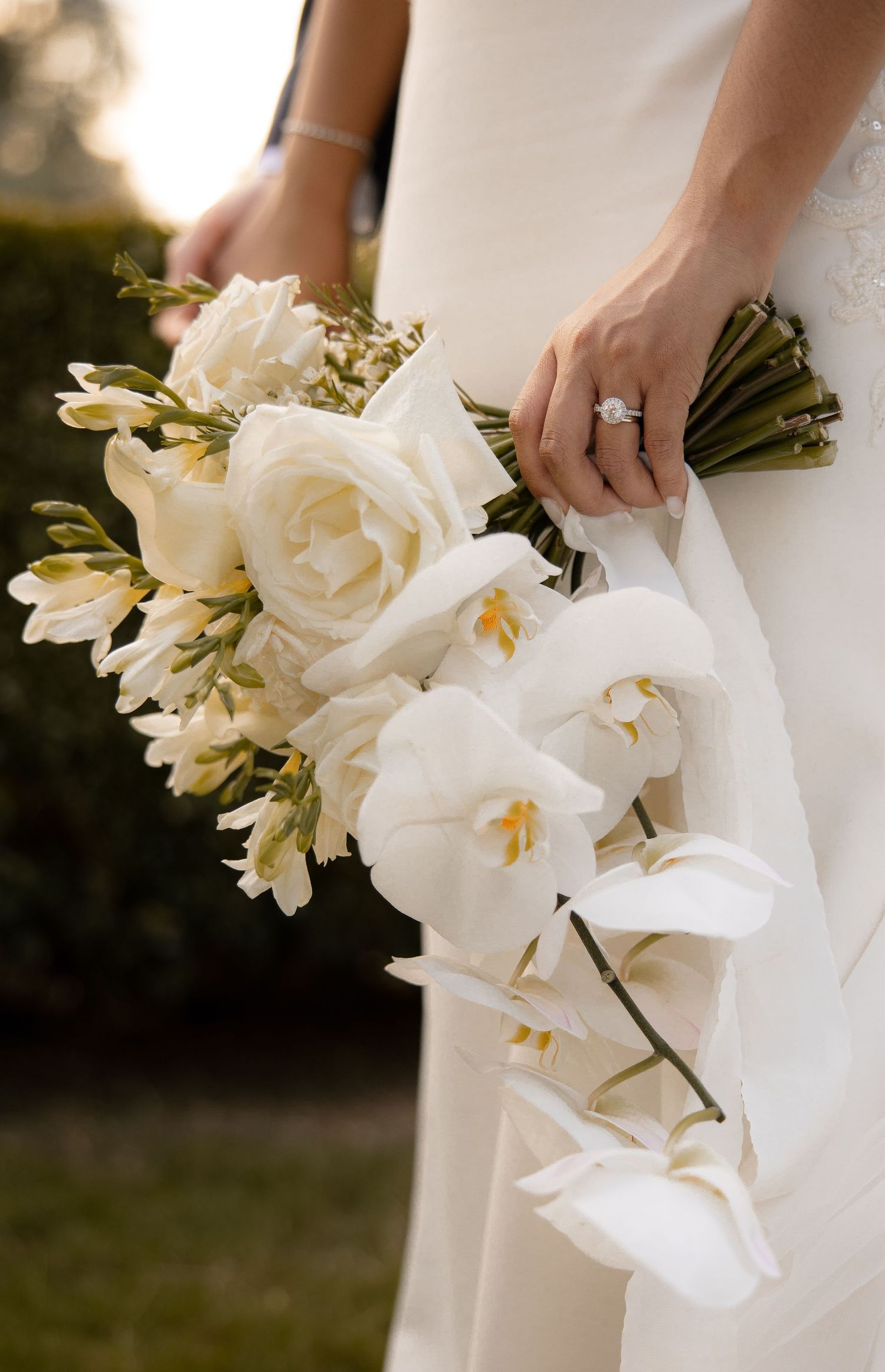 An elegant white orchid and rose wedding bouquet held against a white wedding dress.