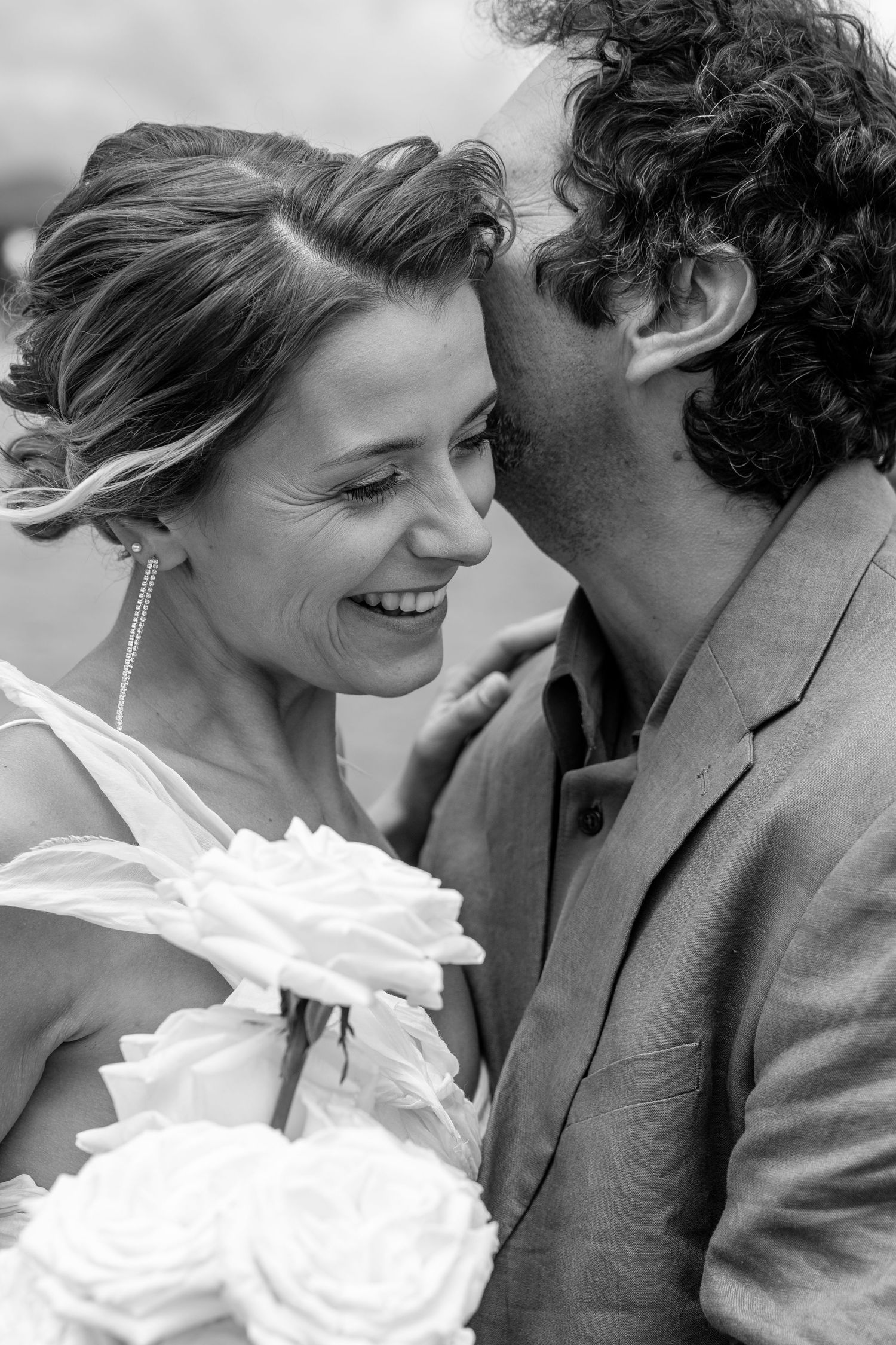 Close-up black and white portrait of a couple sharing a tender romantic moment with white roses.
